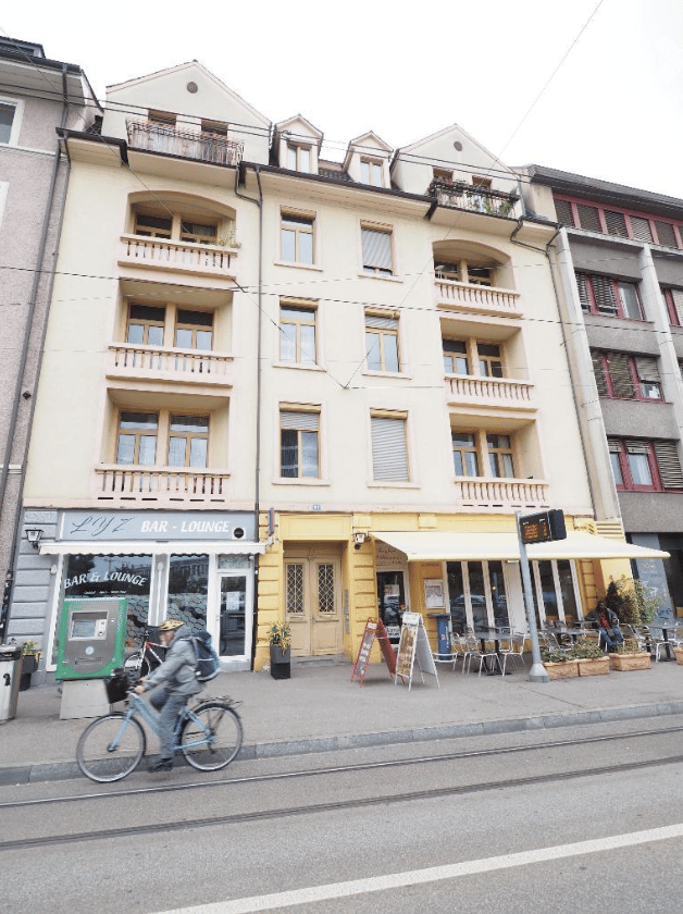 Multi-story residential building with balconies, storefronts including a bar/lounge, and outdoor seating area.