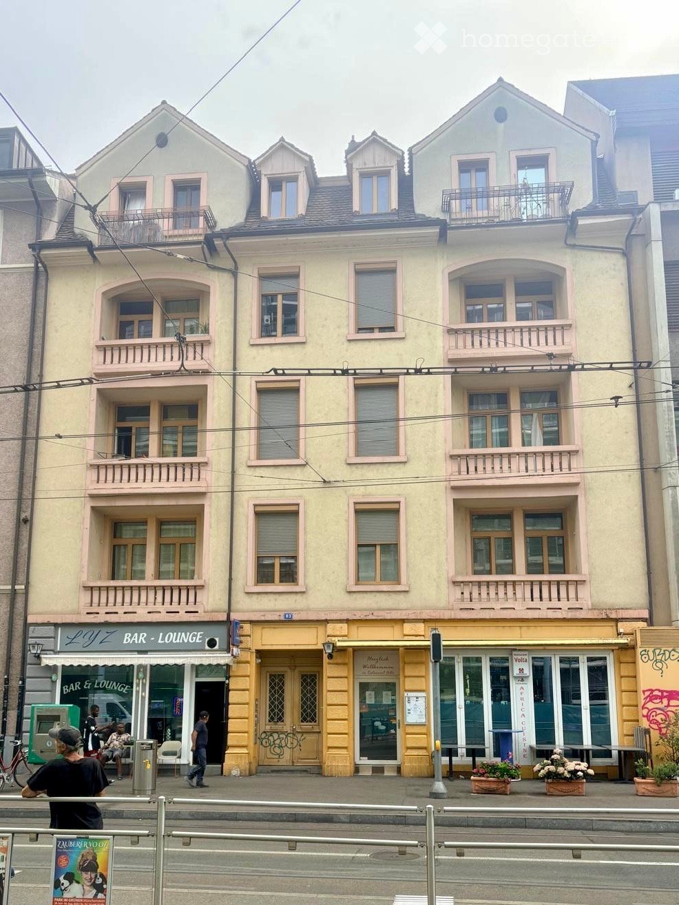 Multi-story building with balconies, storefronts, and signage for "LYZ BAR-LOUNGE" and "Volta" on the ground floor.