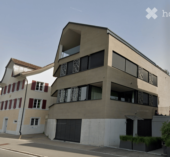 Modern multi-story building with balconies and a garage entrance, featuring contemporary design and large windows.