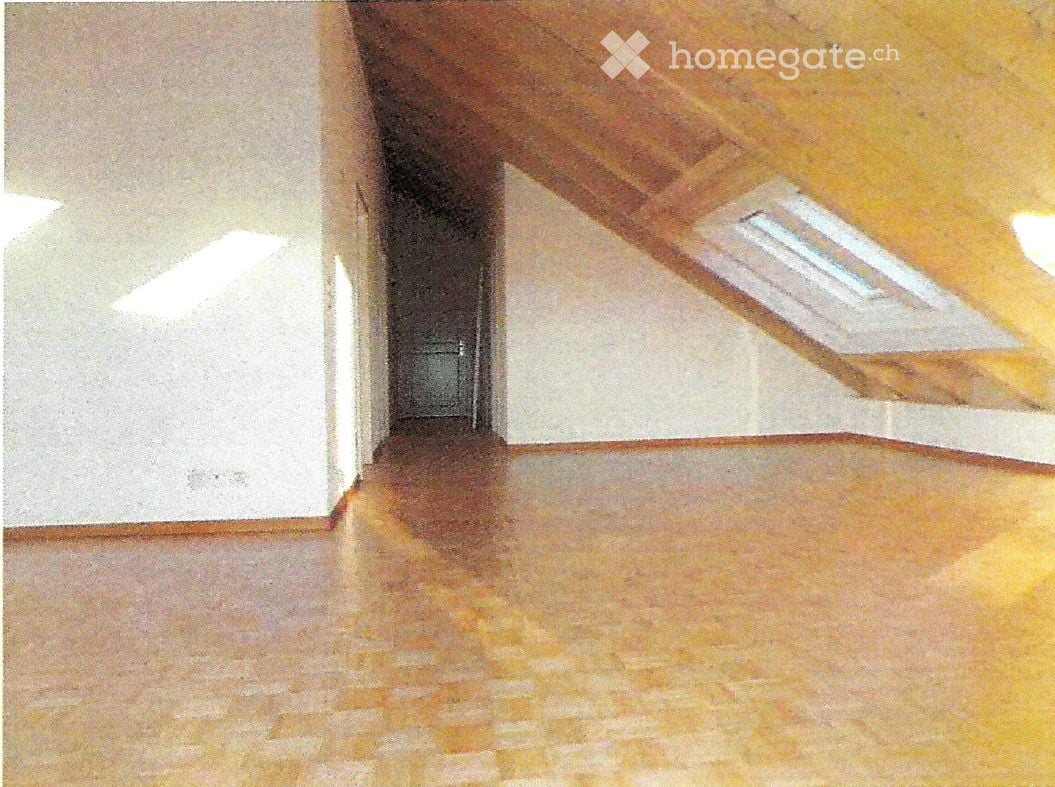 Empty room with wooden flooring and white walls, featuring a visible ceiling beam and a small window at the far end.