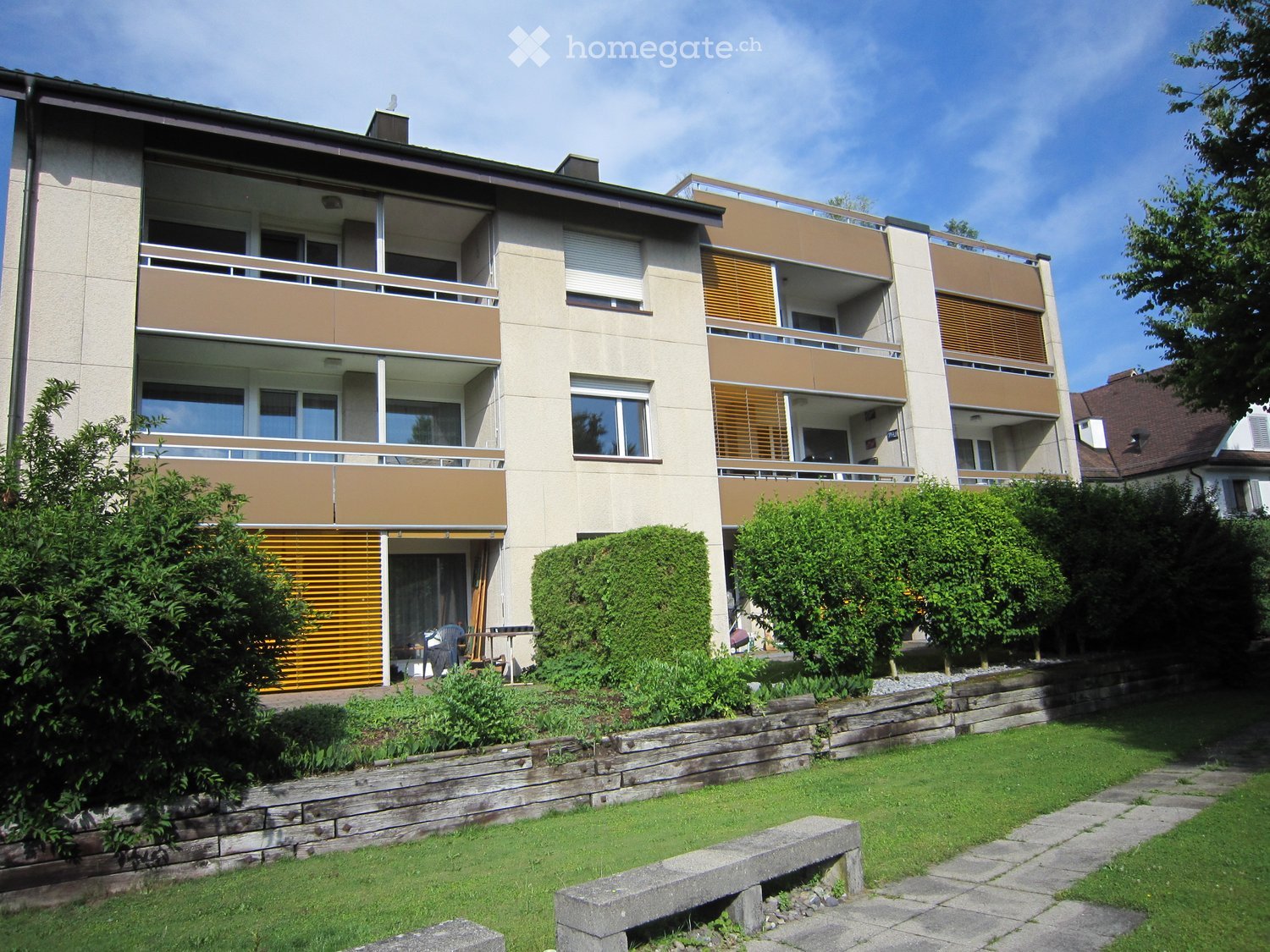 Modern multi-story apartment building with balconies, large windows, and surrounding greenery.