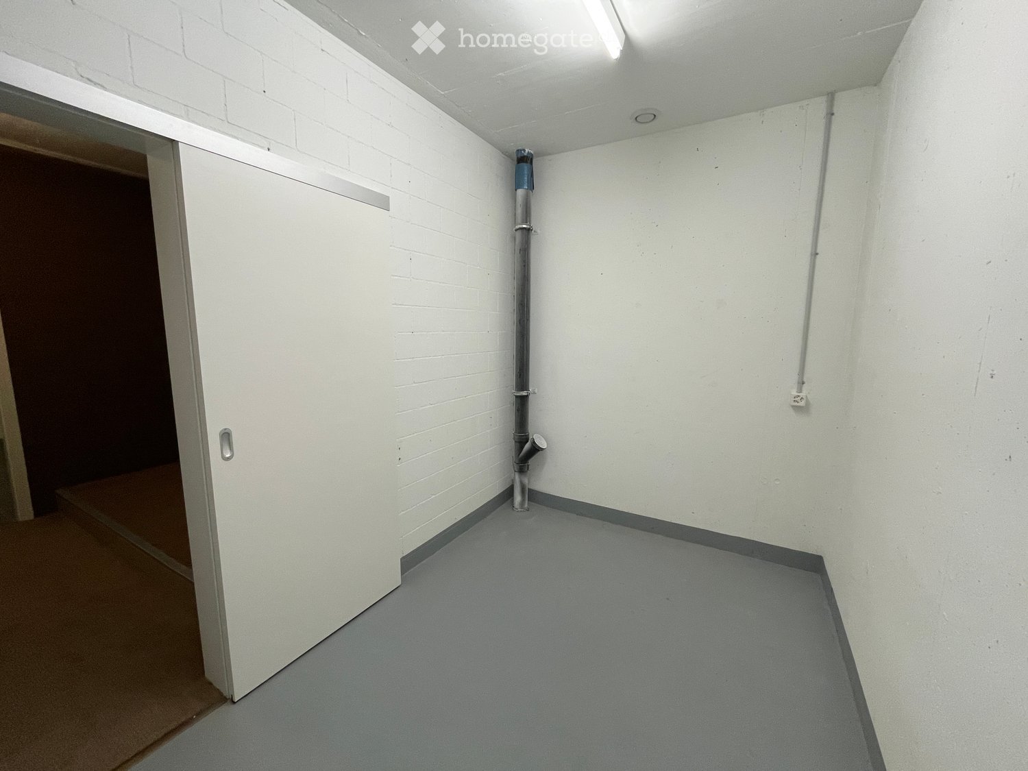 Empty room with white brick walls, grey floor, and a closed white door leading to another space.