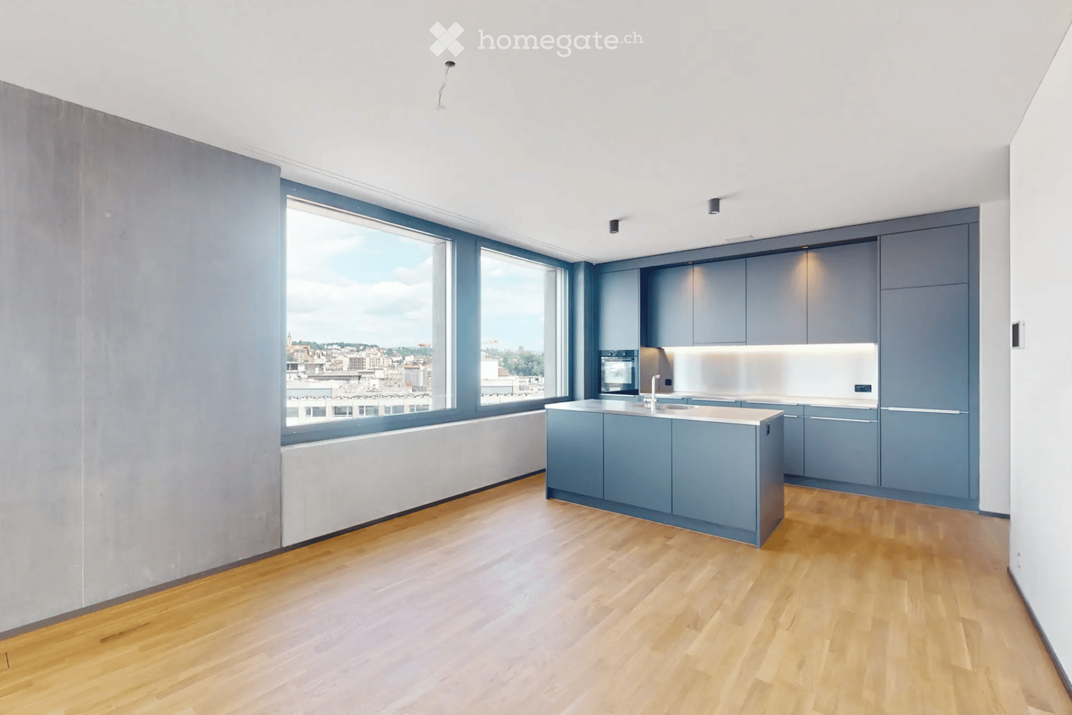 Modern kitchen with grey cabinets, a central island, and large windows offering a city view.