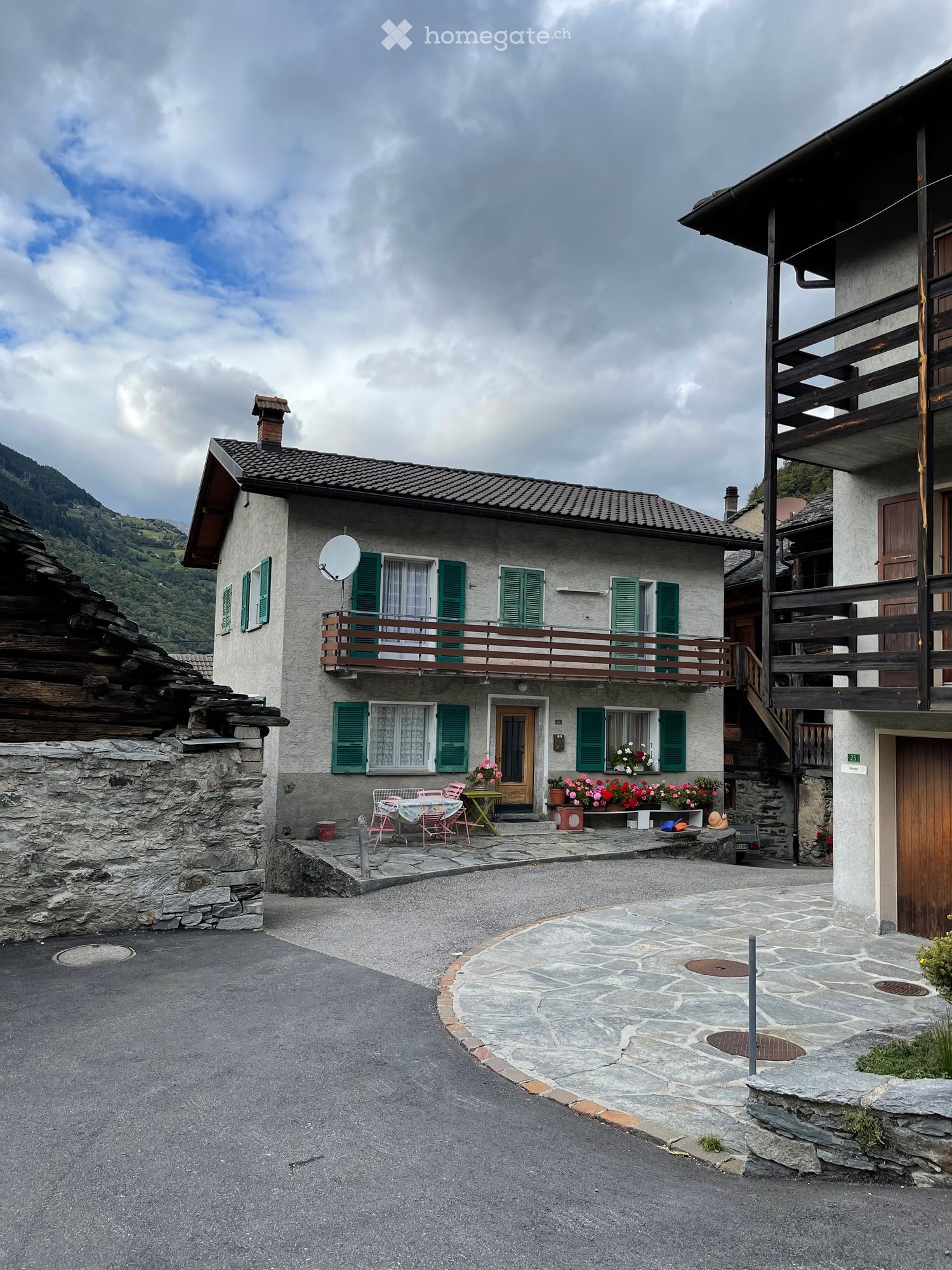 2 story house, green shutters, balcony, satellite dish, garden with flowers, stone wall, paved driveway