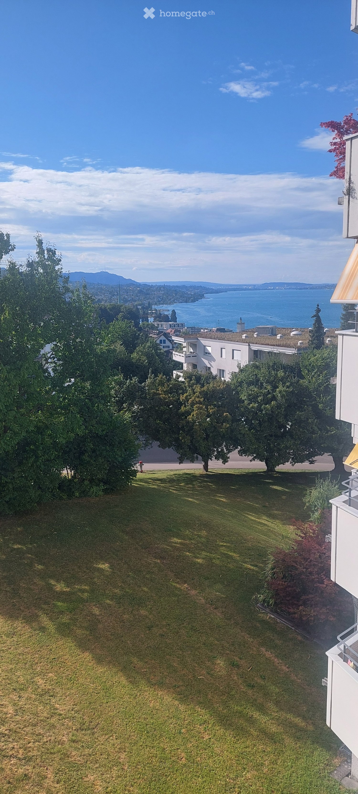 Lush green lawn with trees and shrubs, overlooking a body of water and distant mountains.