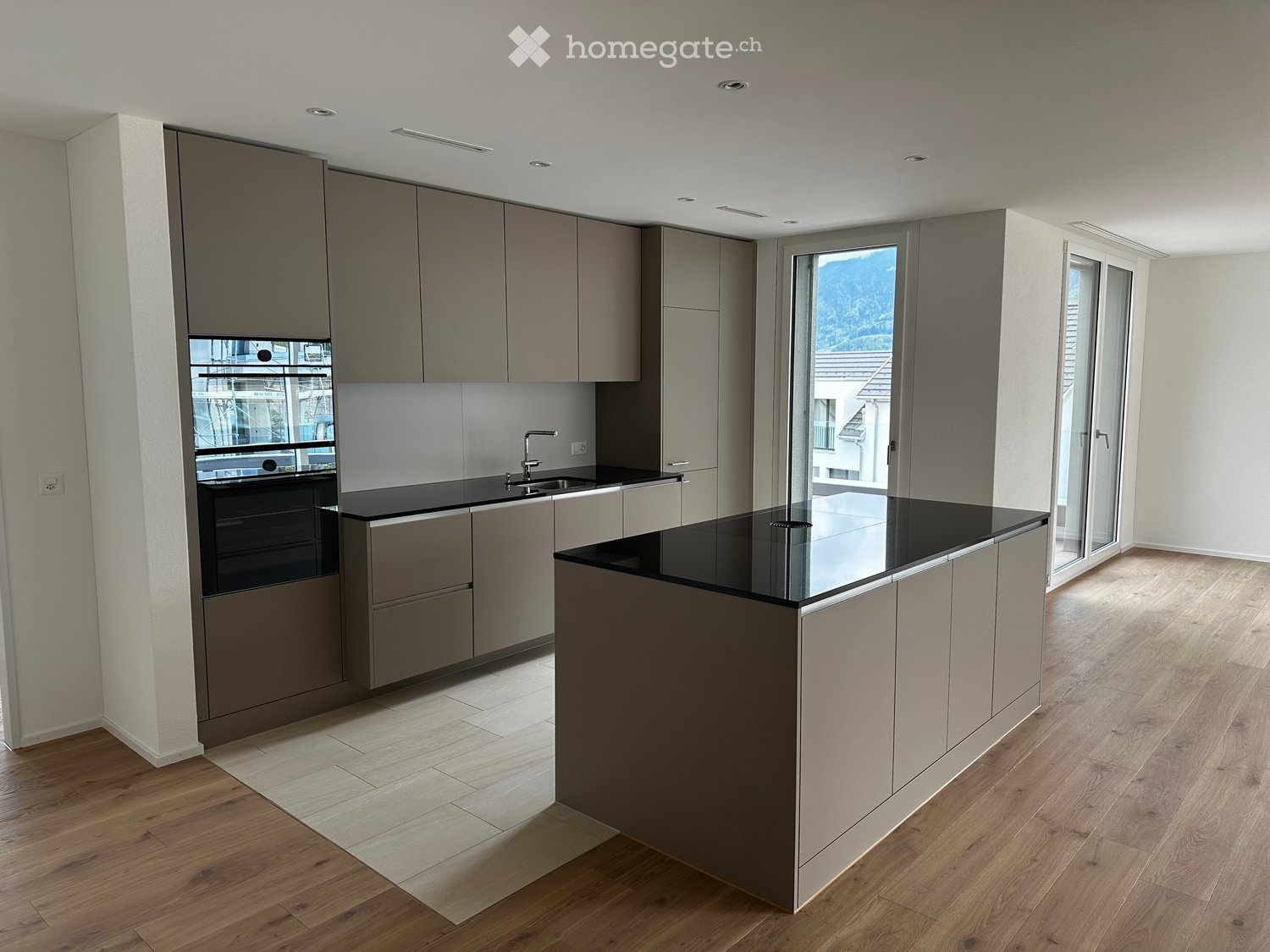 Modern kitchen with grey cabinets, black countertops, a central island, and large windows offering a scenic view.