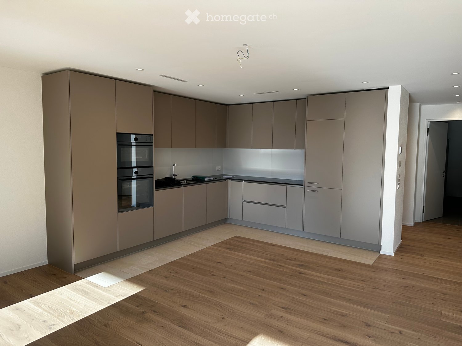 Modern kitchen with light wood flooring, grey cabinets, and a built-in oven. A small white table is placed in the center of the room.