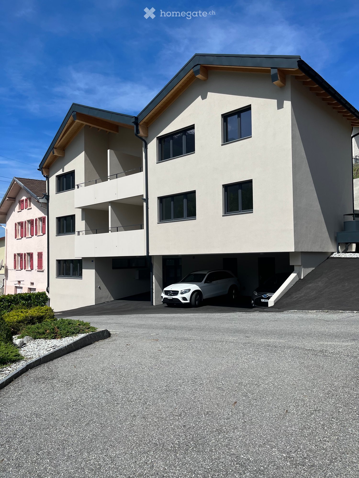 Modern two-story house with white exterior, large windows, and a covered garage with two cars parked inside.
