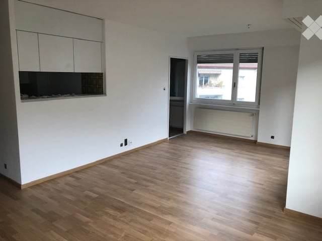Empty room with wooden flooring, white walls, built-in cabinets, and a window with a view of the outside.