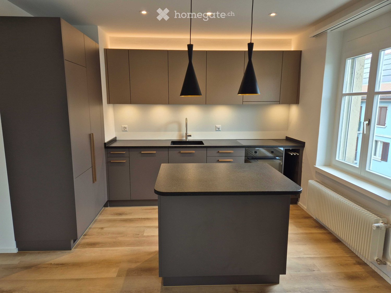 Modern kitchen with grey cabinets, island, pendant lights, and a sink.