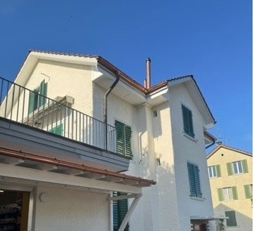Two-story white building with green shutters, balcony, and chimney.