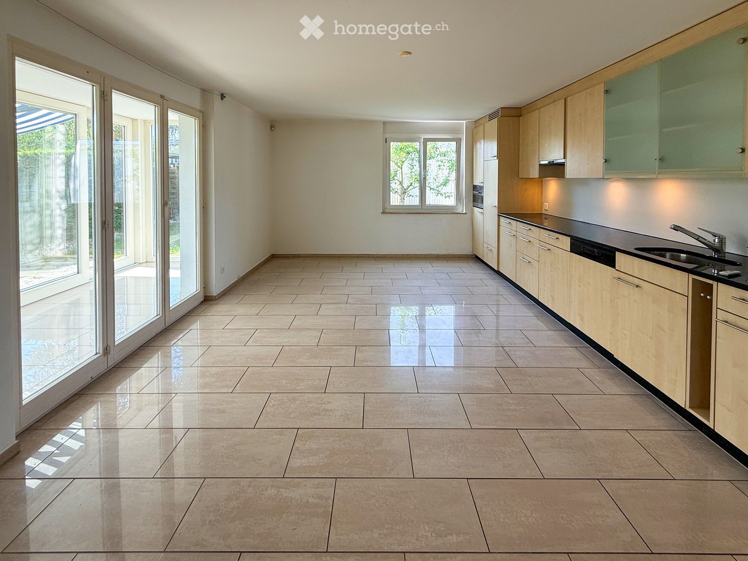 Empty kitchen with light wooden cabinets, black countertops, and large sliding glass doors leading to an outdoor area.