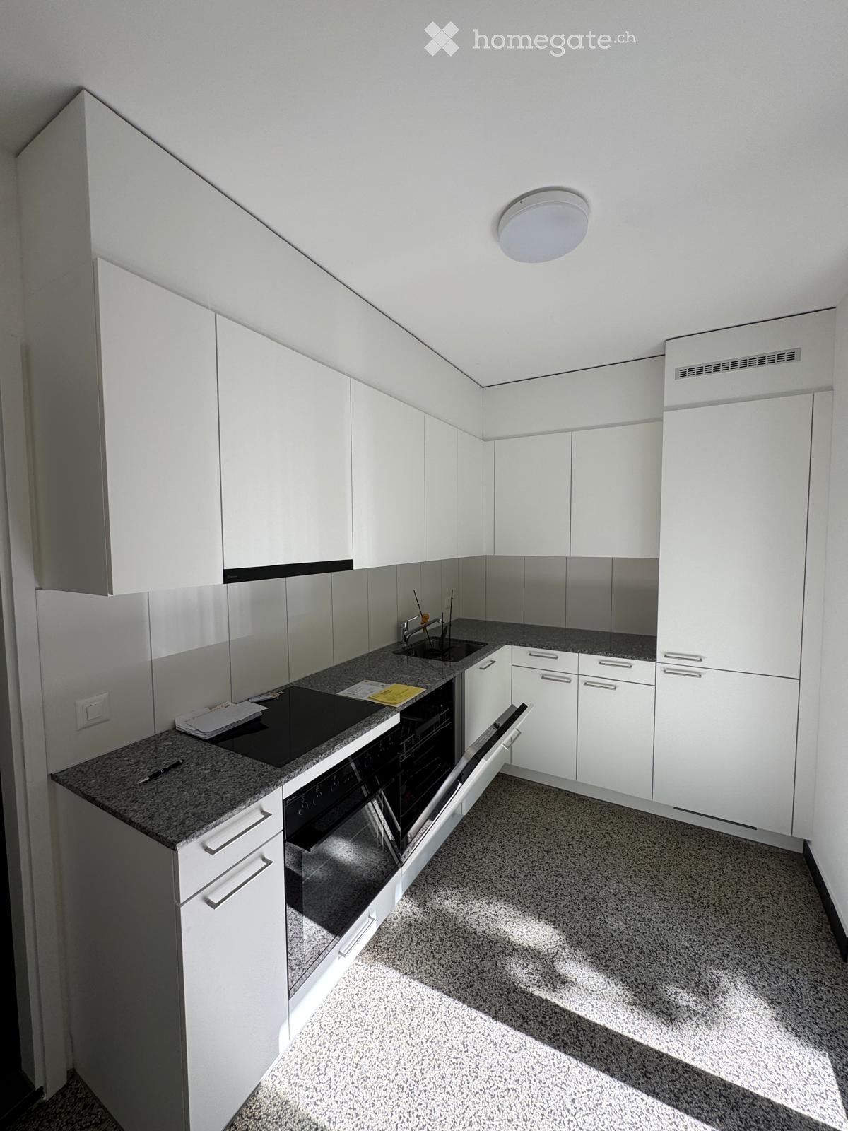 Modern kitchen with white cabinets, granite countertop, built-in oven, and sink.