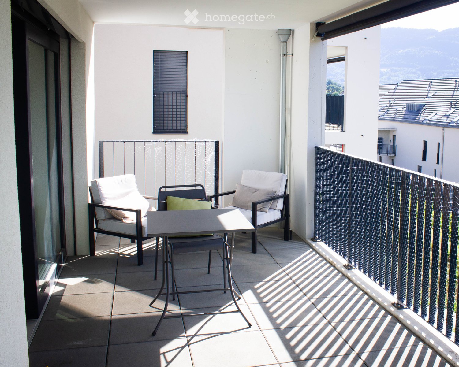 Balcony with tiled floor, white walls, and a view of the surrounding area. Features a sofa, two chairs, and a small table.