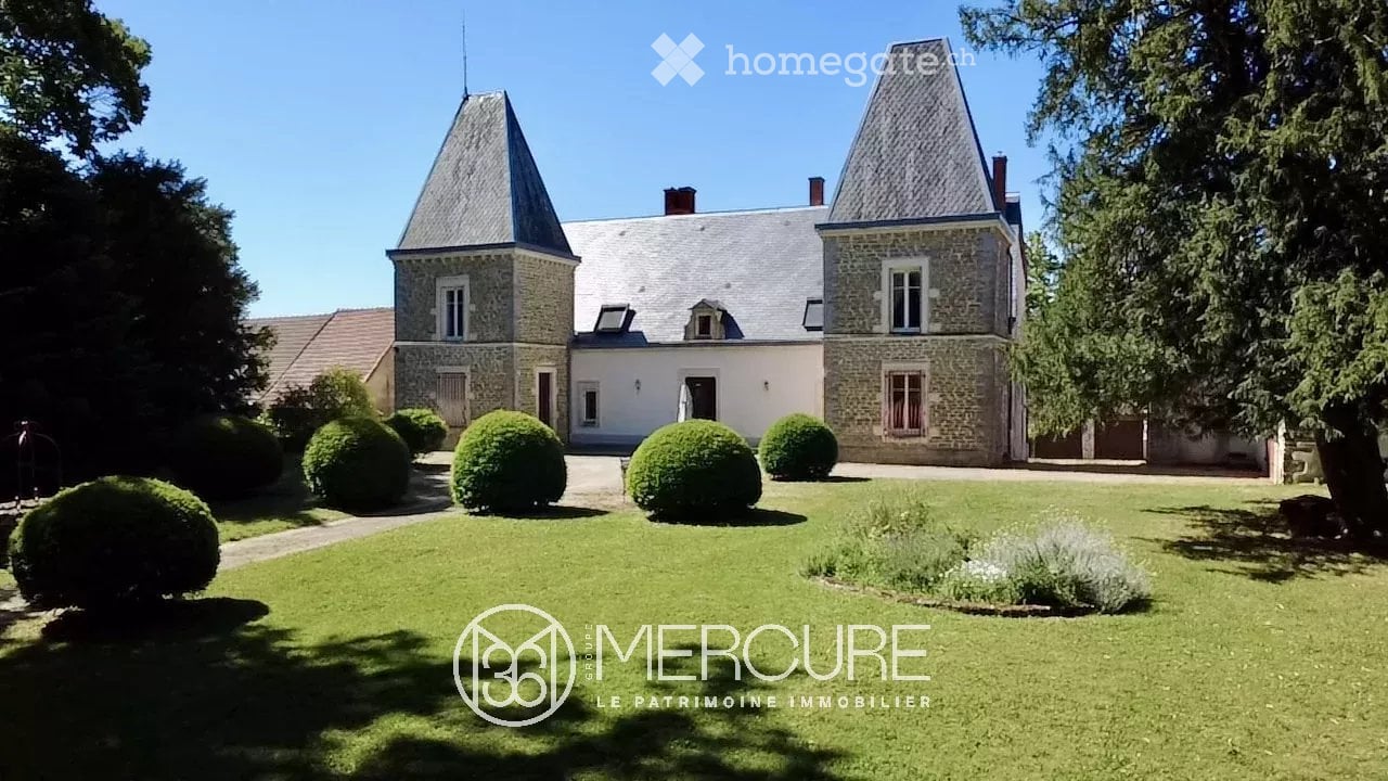 A large, elegant stone manor house with a grey slate roof, multiple chimneys, and symmetrical design, surrounded by a well-maintained lawn and manicured hedges.