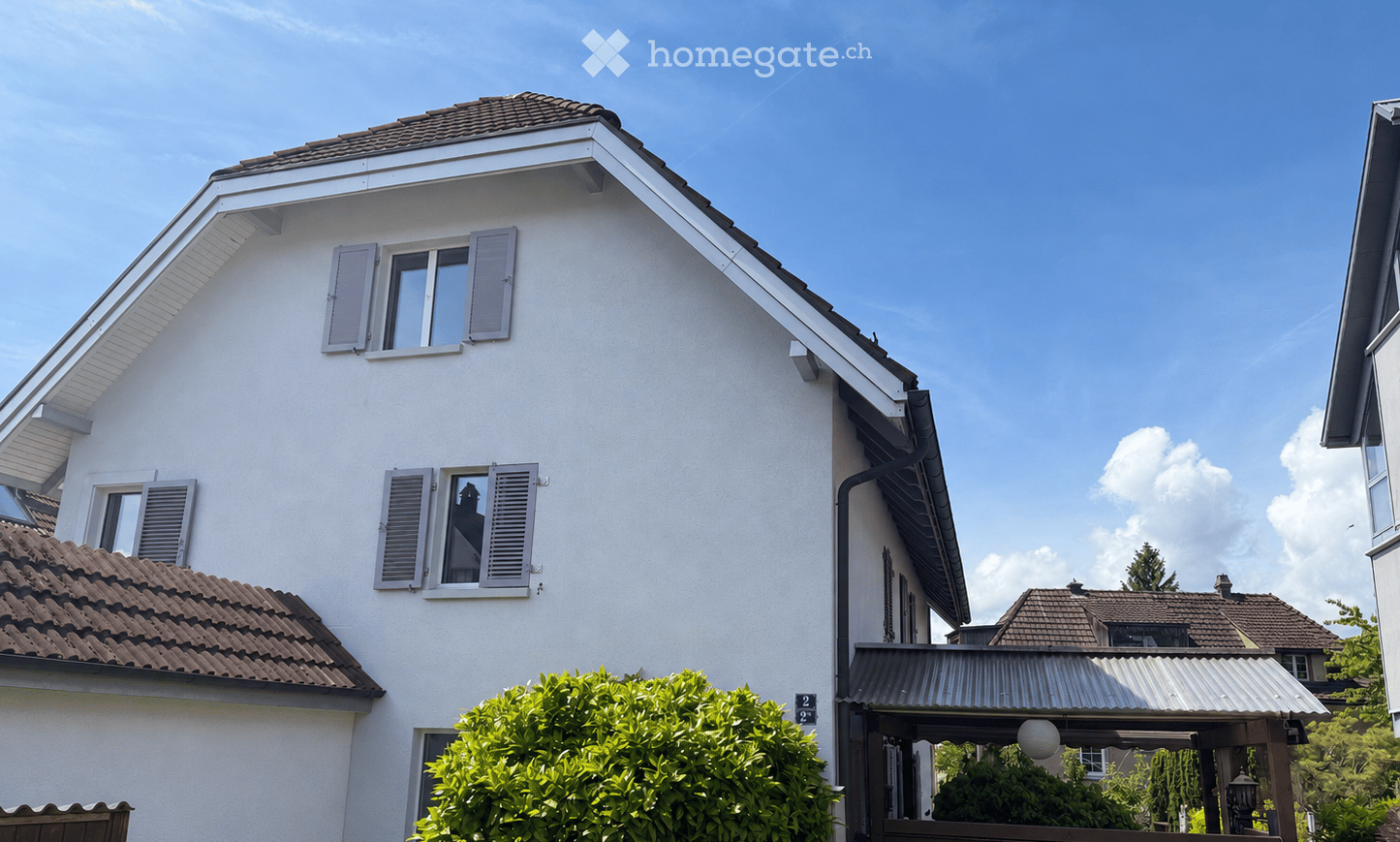 House. Two-story house with white exterior, brown tiled roof, multiple windows with shutters, and a small garden area in front.