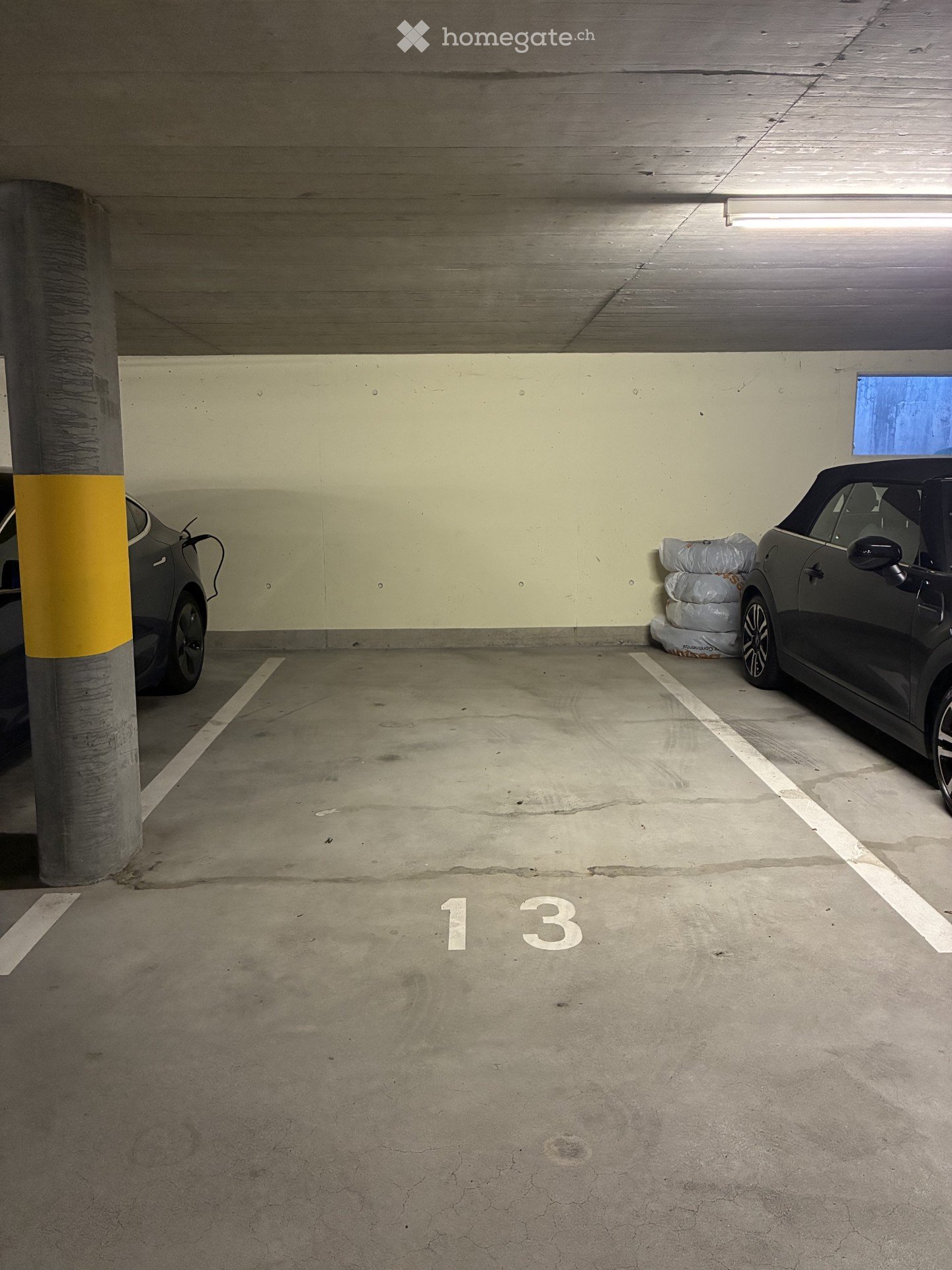 Underground parking area with two parked cars, marked parking spaces, and a concrete pillar.