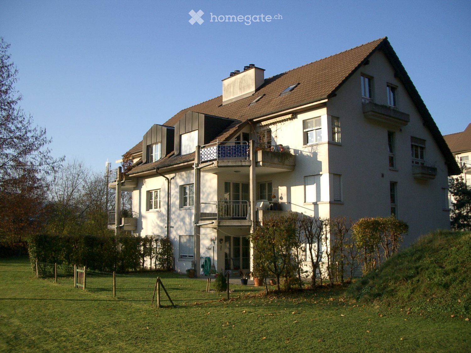 Two-story house with white exterior, multiple windows, balconies, and a well-maintained lawn in front.