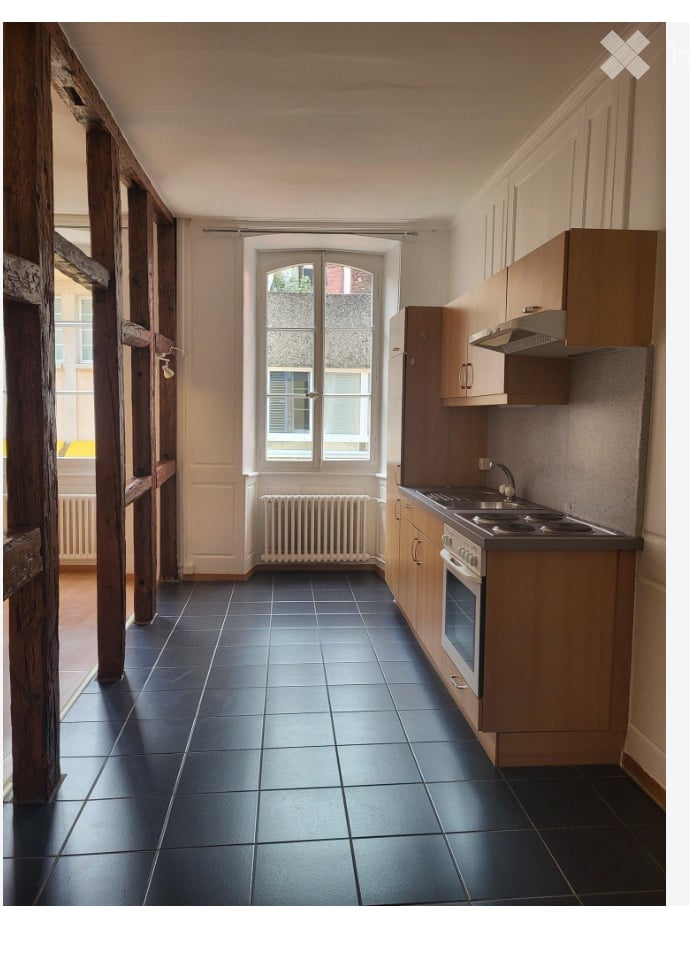 Modern kitchen with dark tiled floor, light wooden cabinets, built-in oven, sink, and radiator under window.