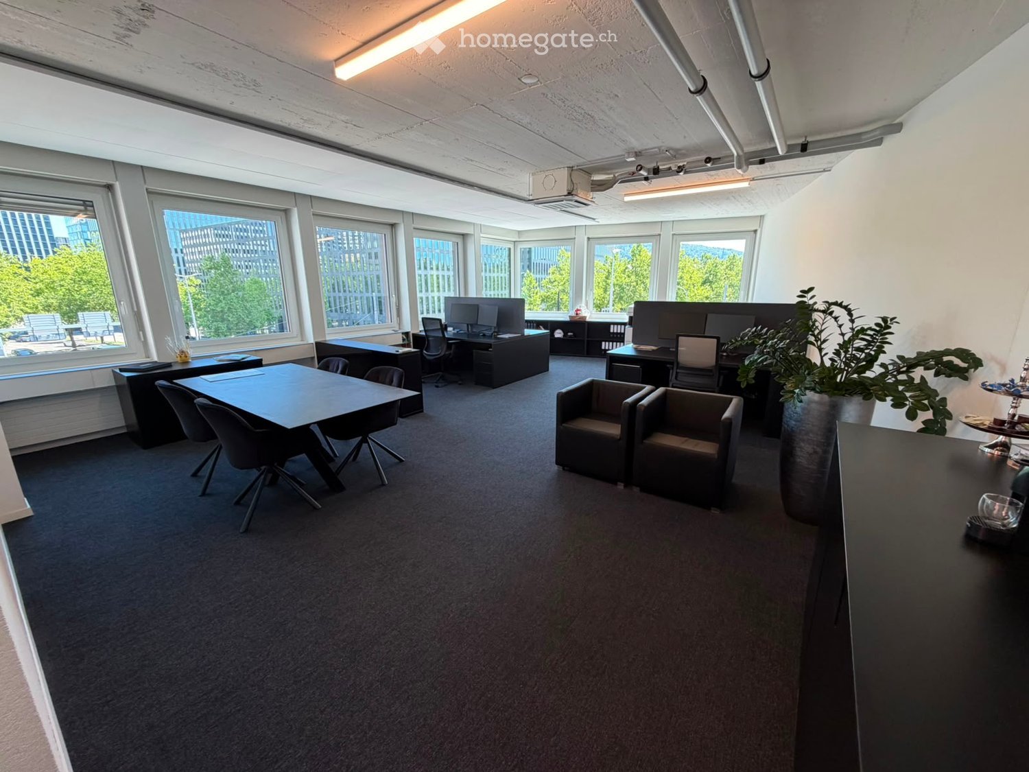 Modern office space with large windows, desks, chairs, and a meeting table.