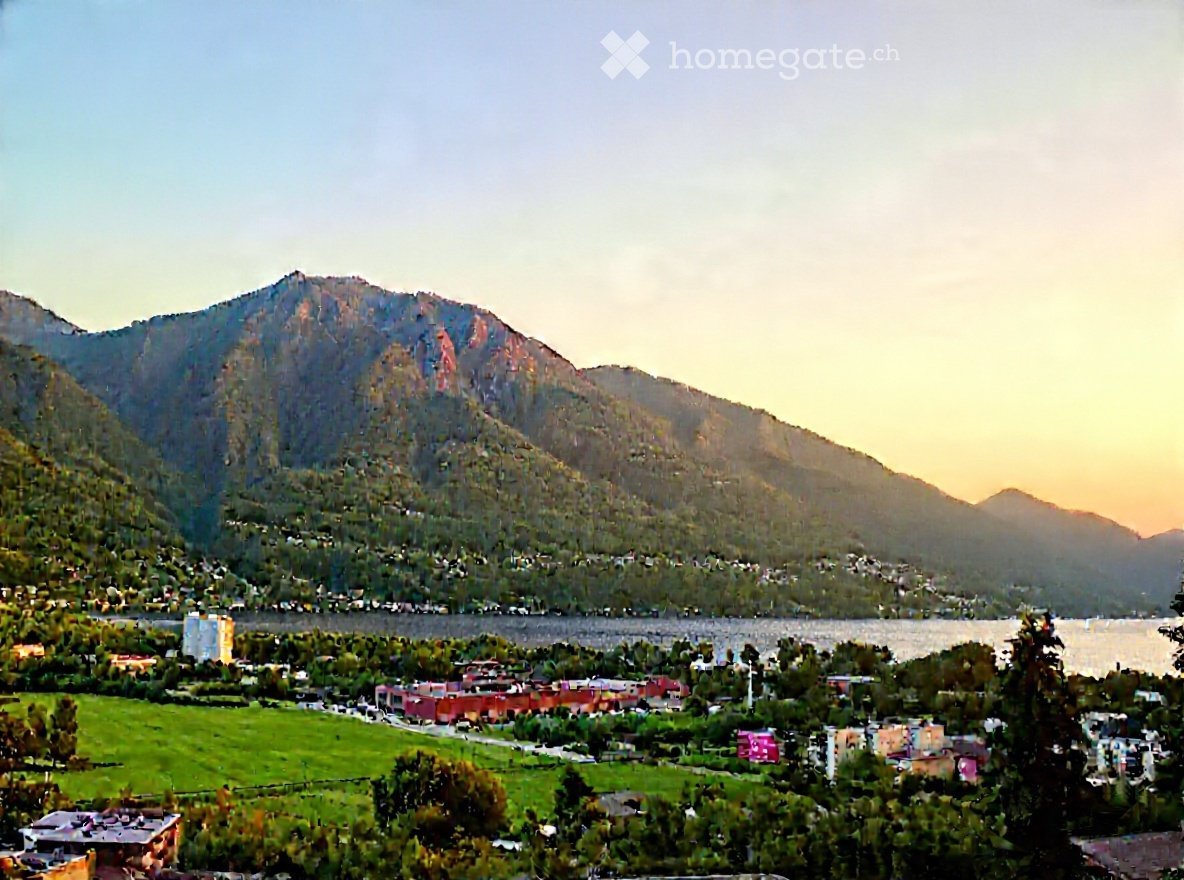 Panoramic view of a town nestled in a valley surrounded by mountains, with a river running through the area and green fields in the foreground.