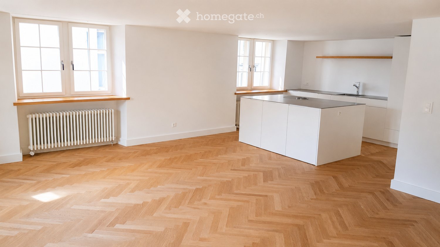 Modern kitchen with white cabinets, a central island, and herringbone wooden flooring. Features a radiator under a large window and a sink with a modern faucet.