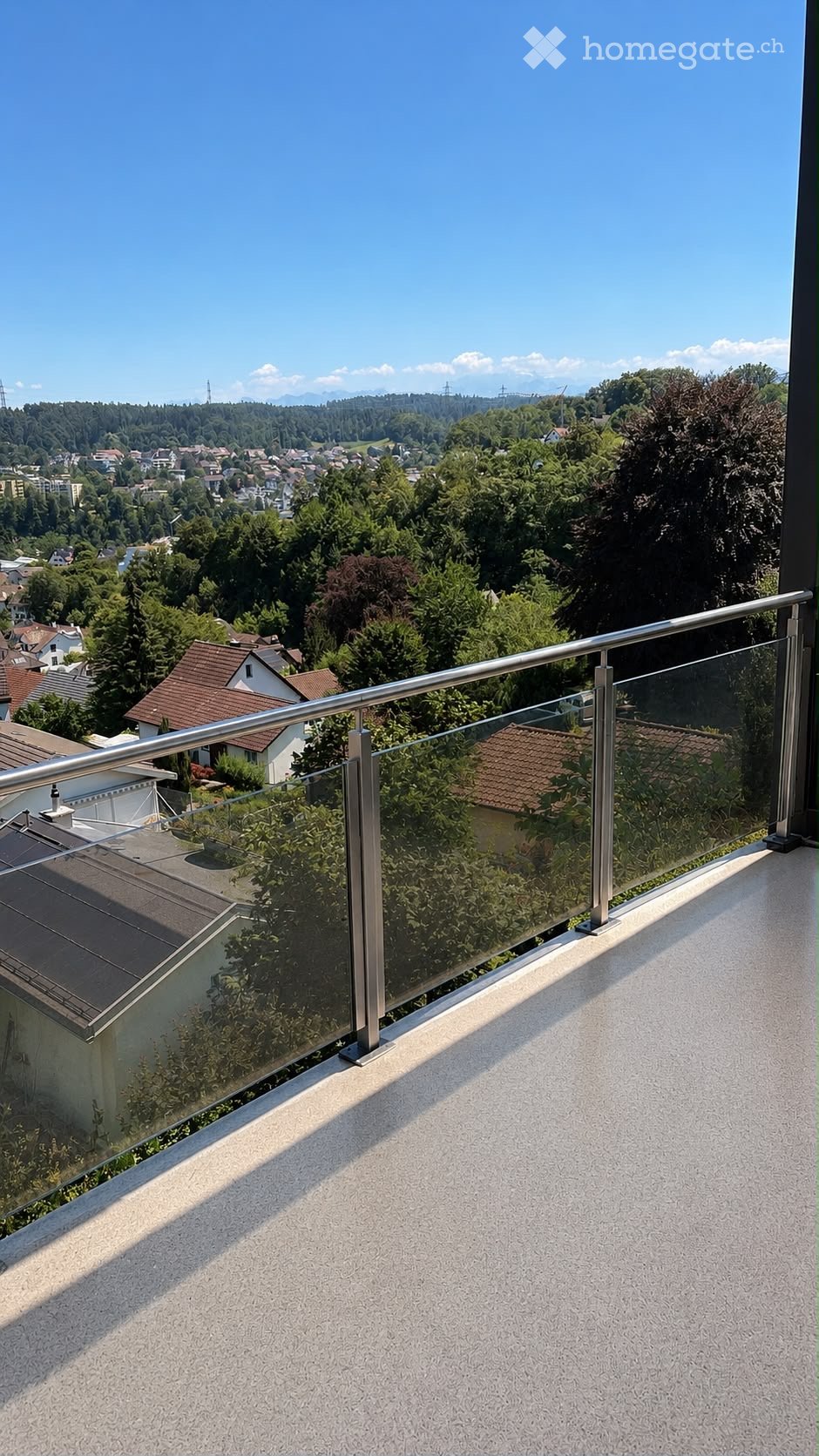 Balcony with glass railing and metal balustrade, overlooking a suburban area with houses and trees.