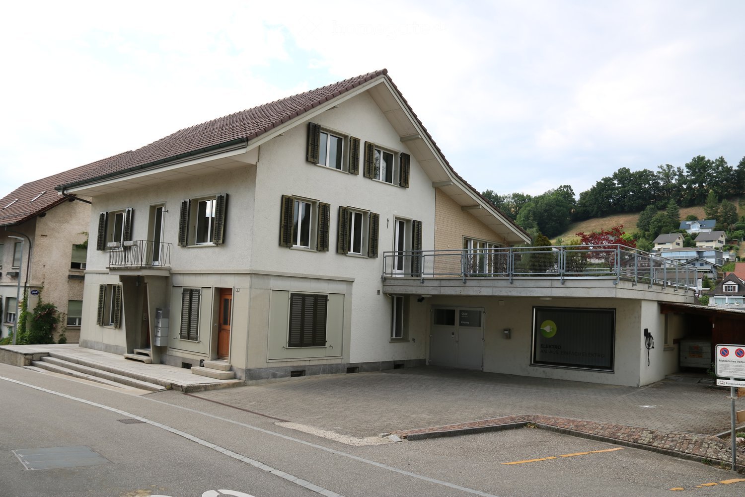 Two-story residential building with white exterior, multiple windows, balconies, and a garage entrance.