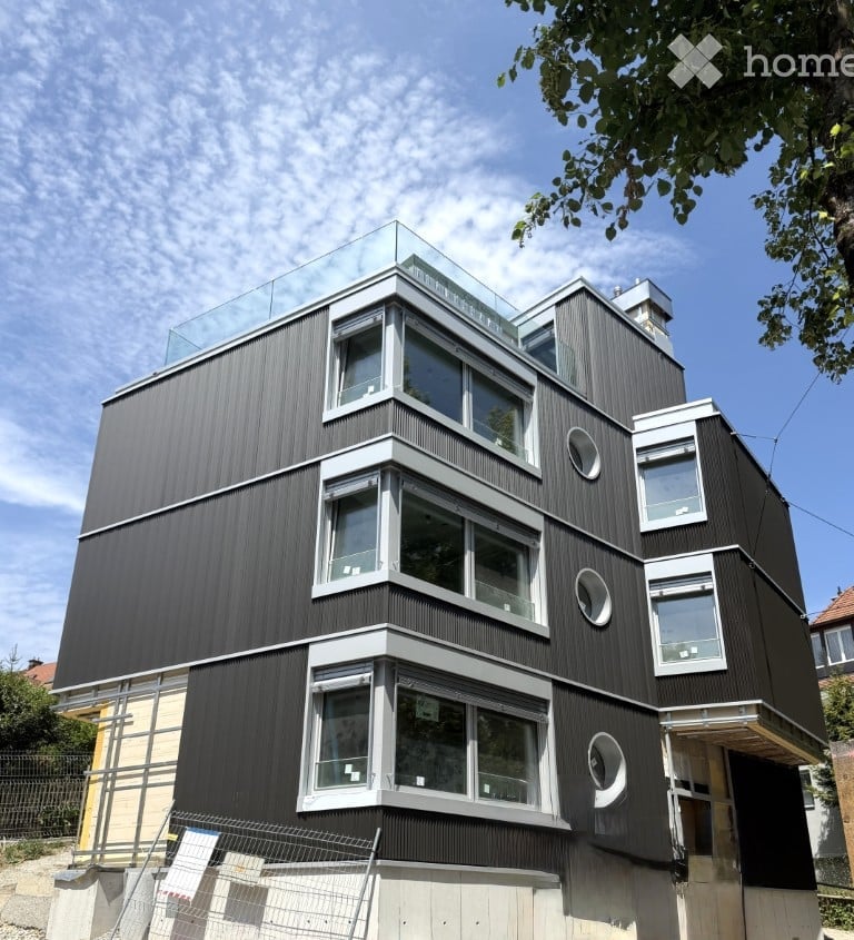 Modern, multi-story building with dark wood siding, large windows, and a glass rooftop terrace.