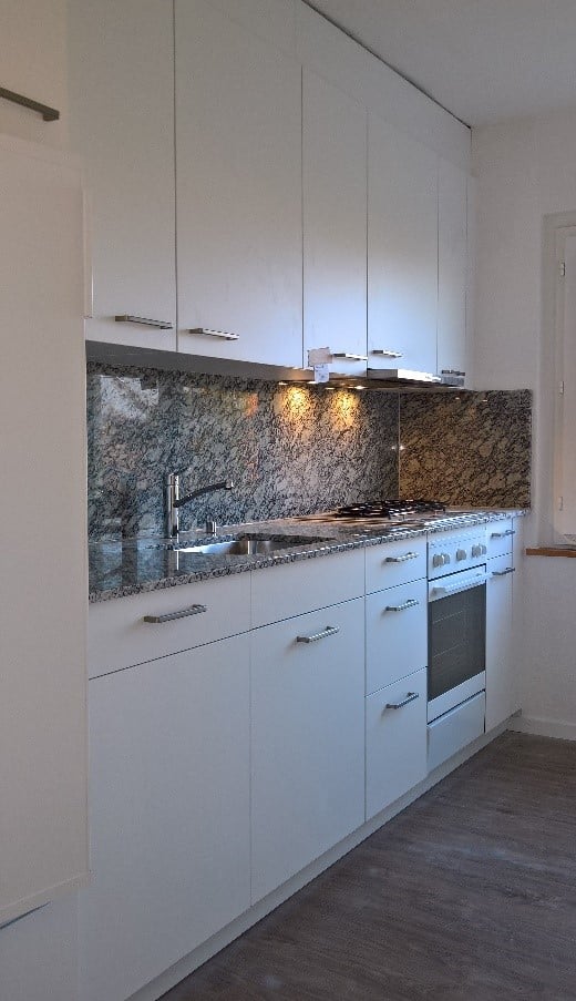 Modern kitchen with white cabinets, granite backsplash, stainless steel sink and stove, and built-in oven.