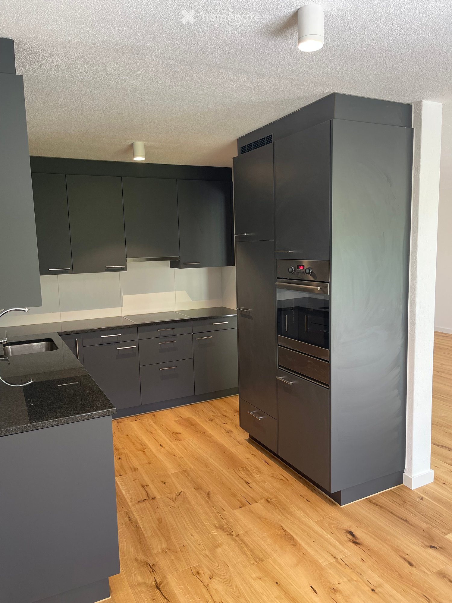 Modern kitchen with dark grey cabinets, stainless steel appliances, and wooden flooring.