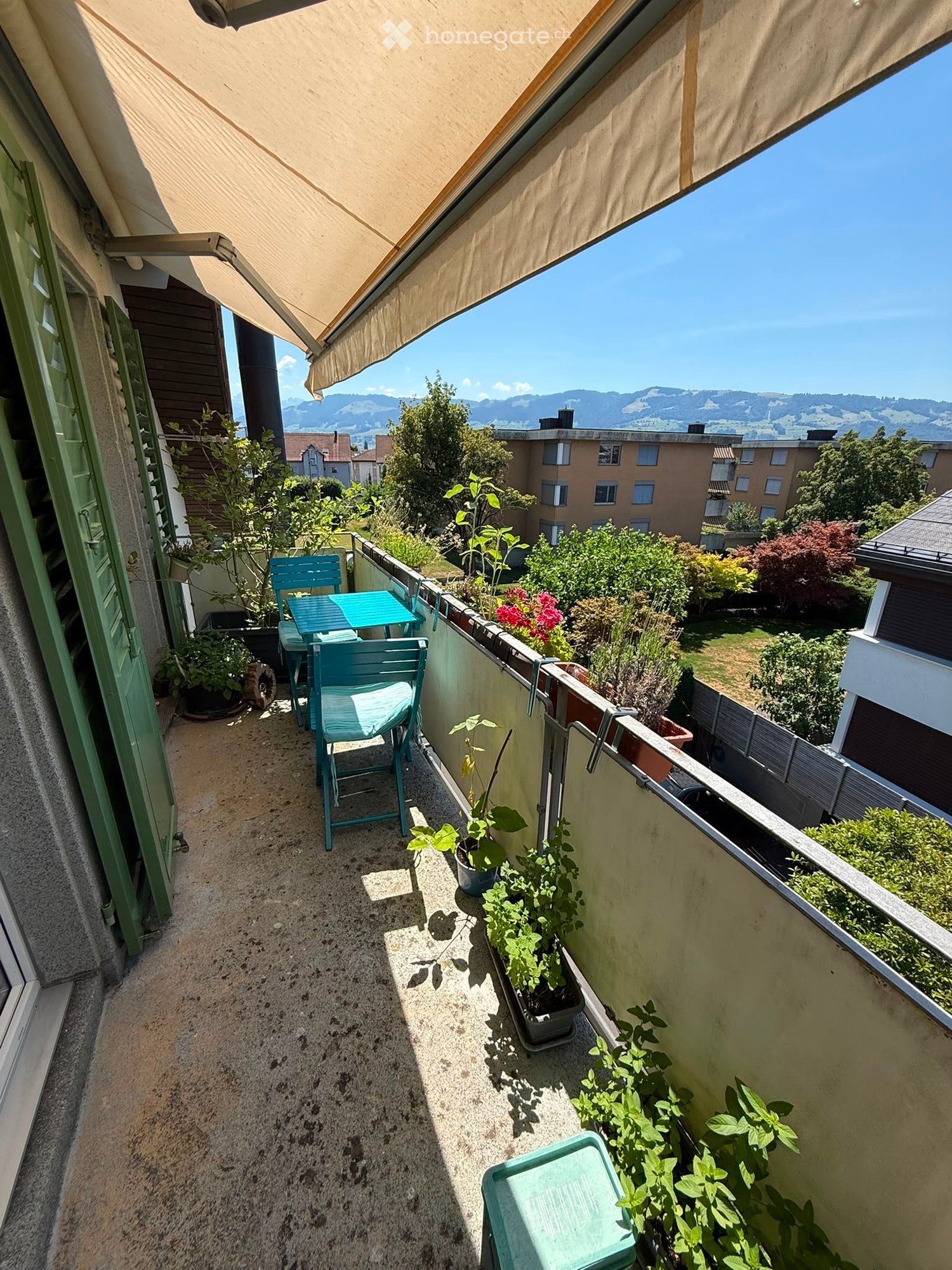 Balcony with a table, chairs, potted plants, and a scenic mountain view.