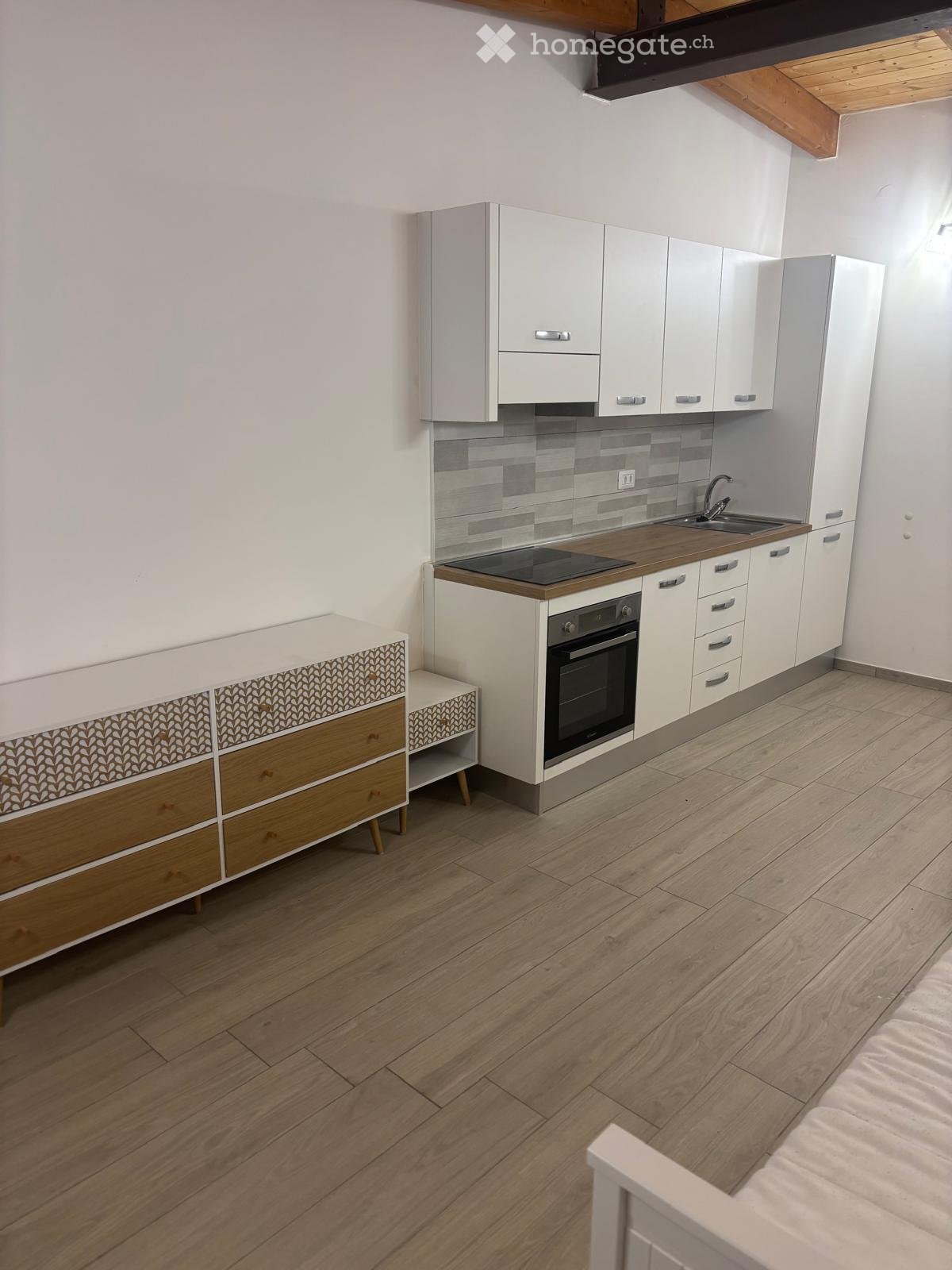 Modern kitchen with white cabinets, wooden countertops, and a built-in oven. Features a sink with a modern faucet and a small wooden side table with drawers.