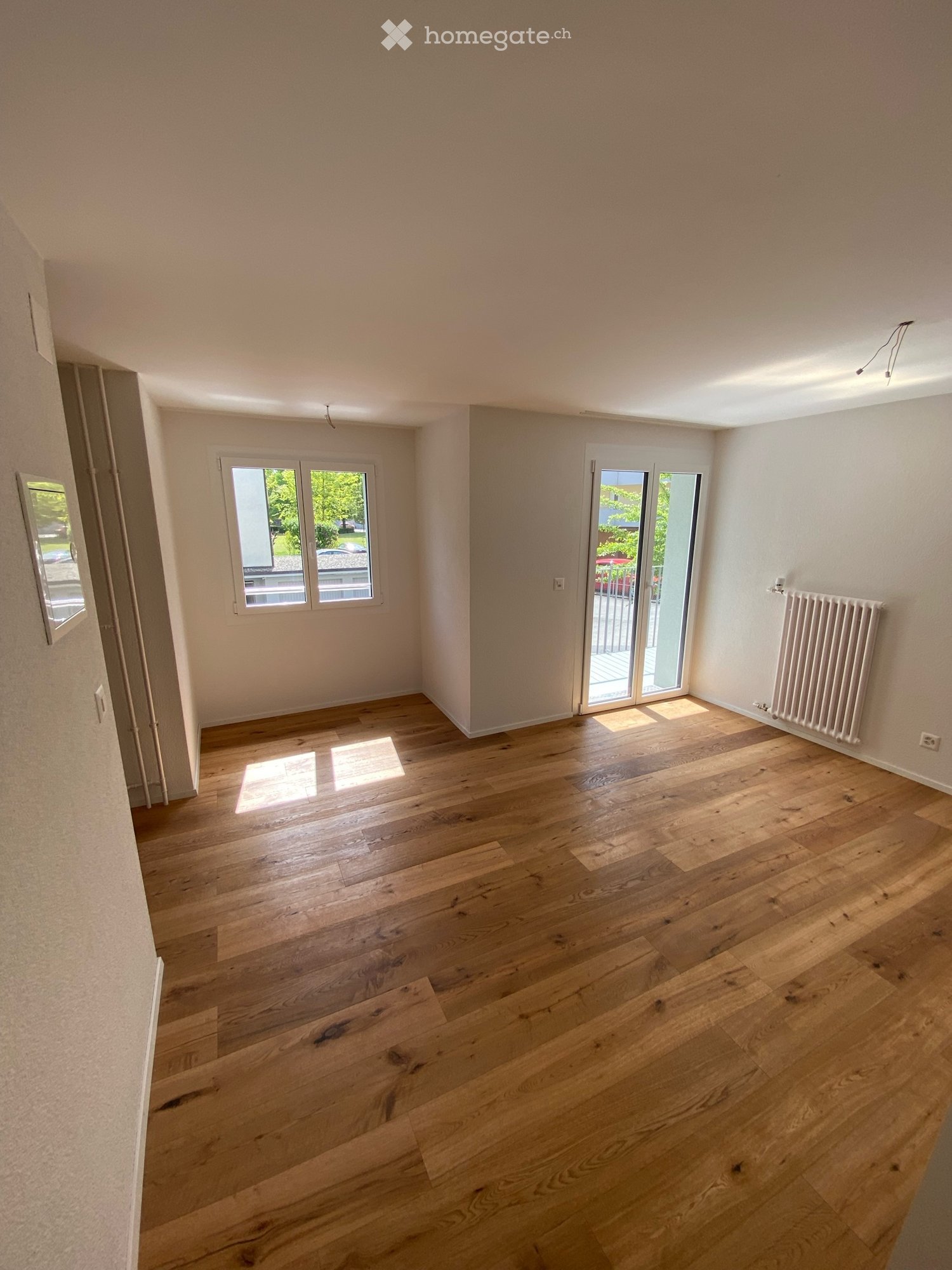 Empty room with wooden flooring, large windows, and a sliding glass door leading to a balcony.