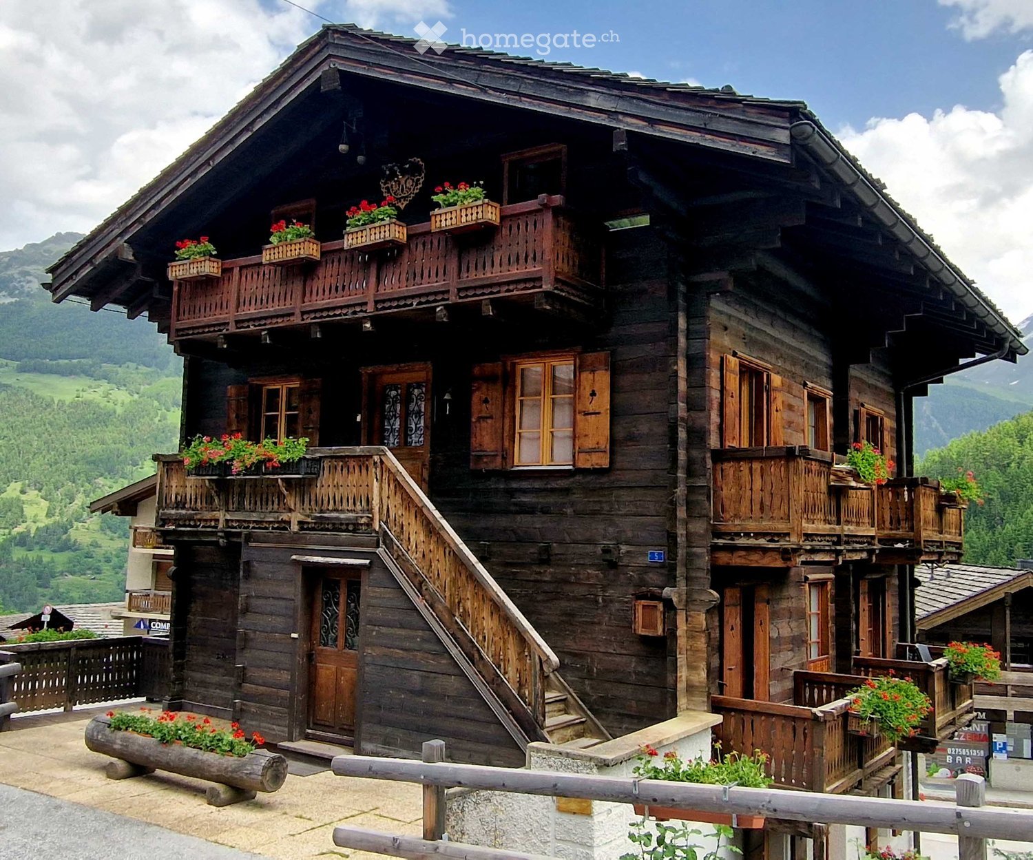 Traditional wooden chalet with multiple balconies, flower boxes, and a staircase leading to the entrance.