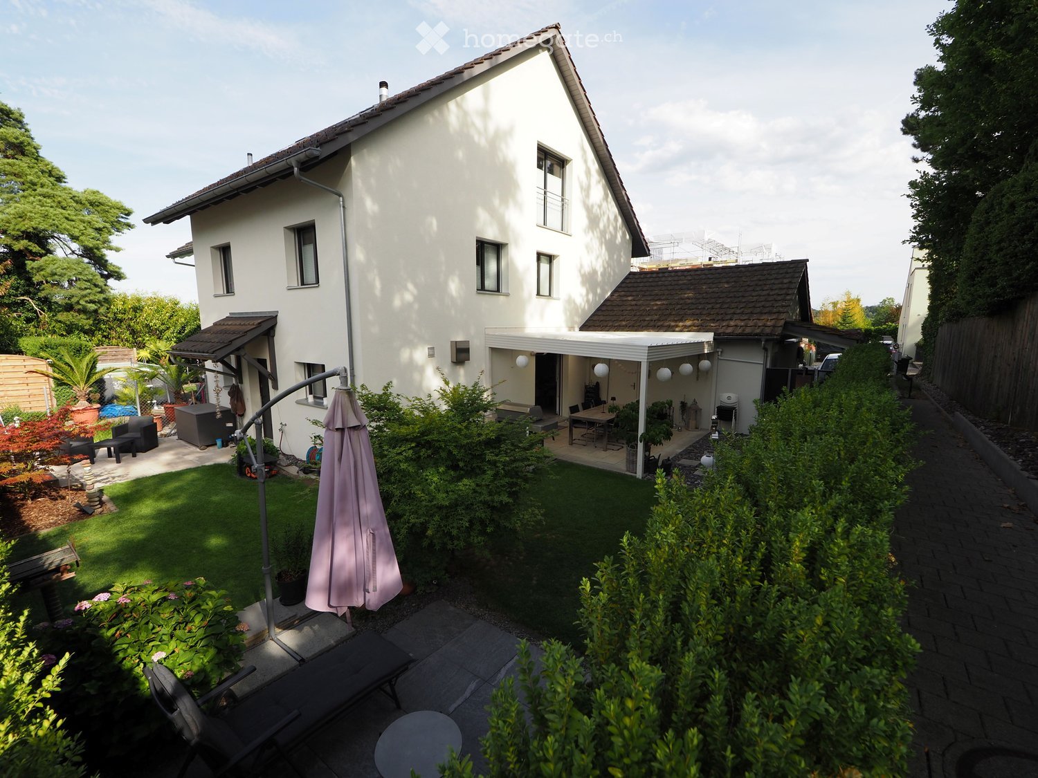 A well-maintained garden with a lawn, patio seating area, outdoor furniture, and a covered patio area connected to the house.