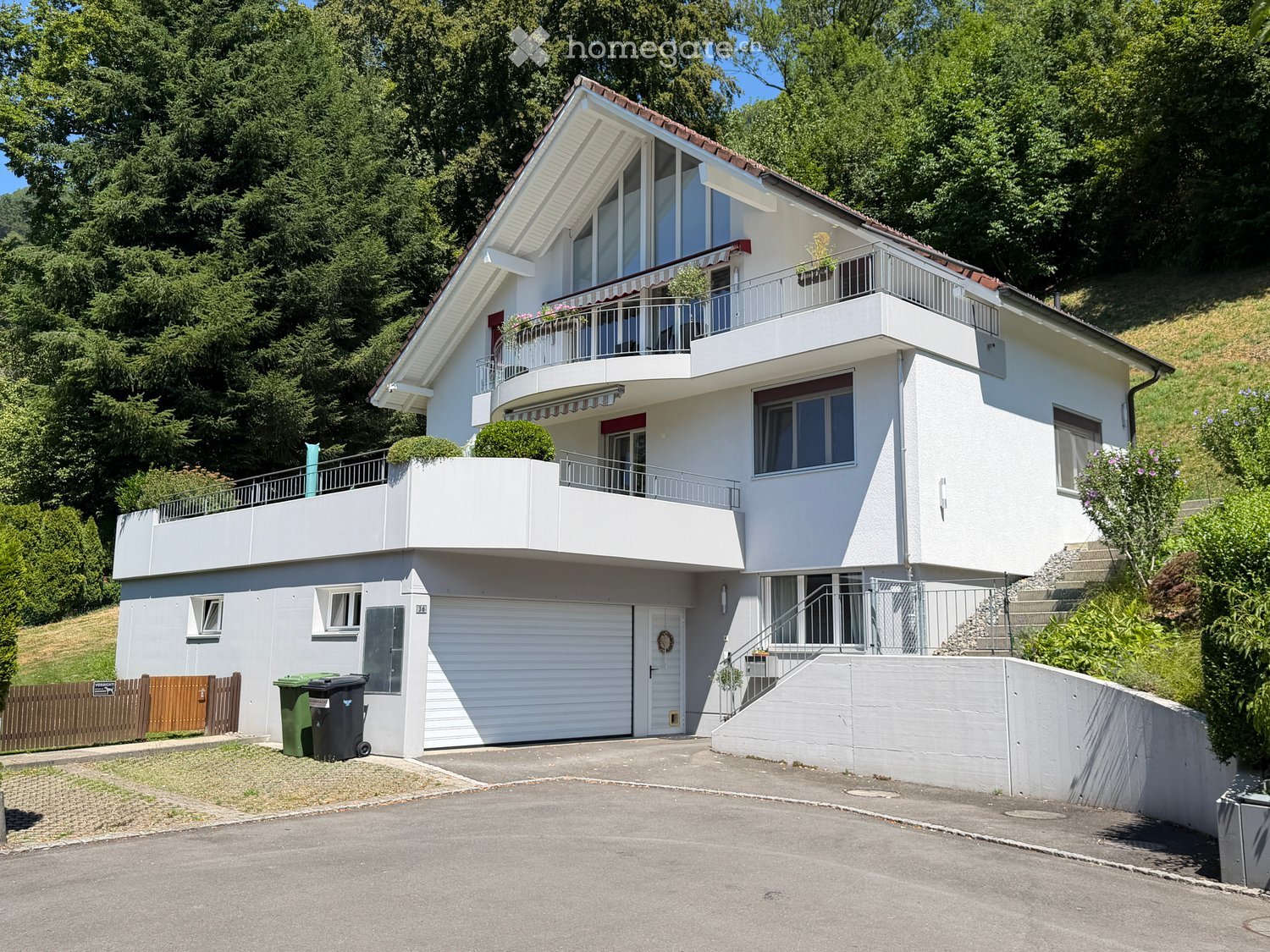 Two-story modern house with white exterior, large windows, balconies, garage, and raised ground floor.