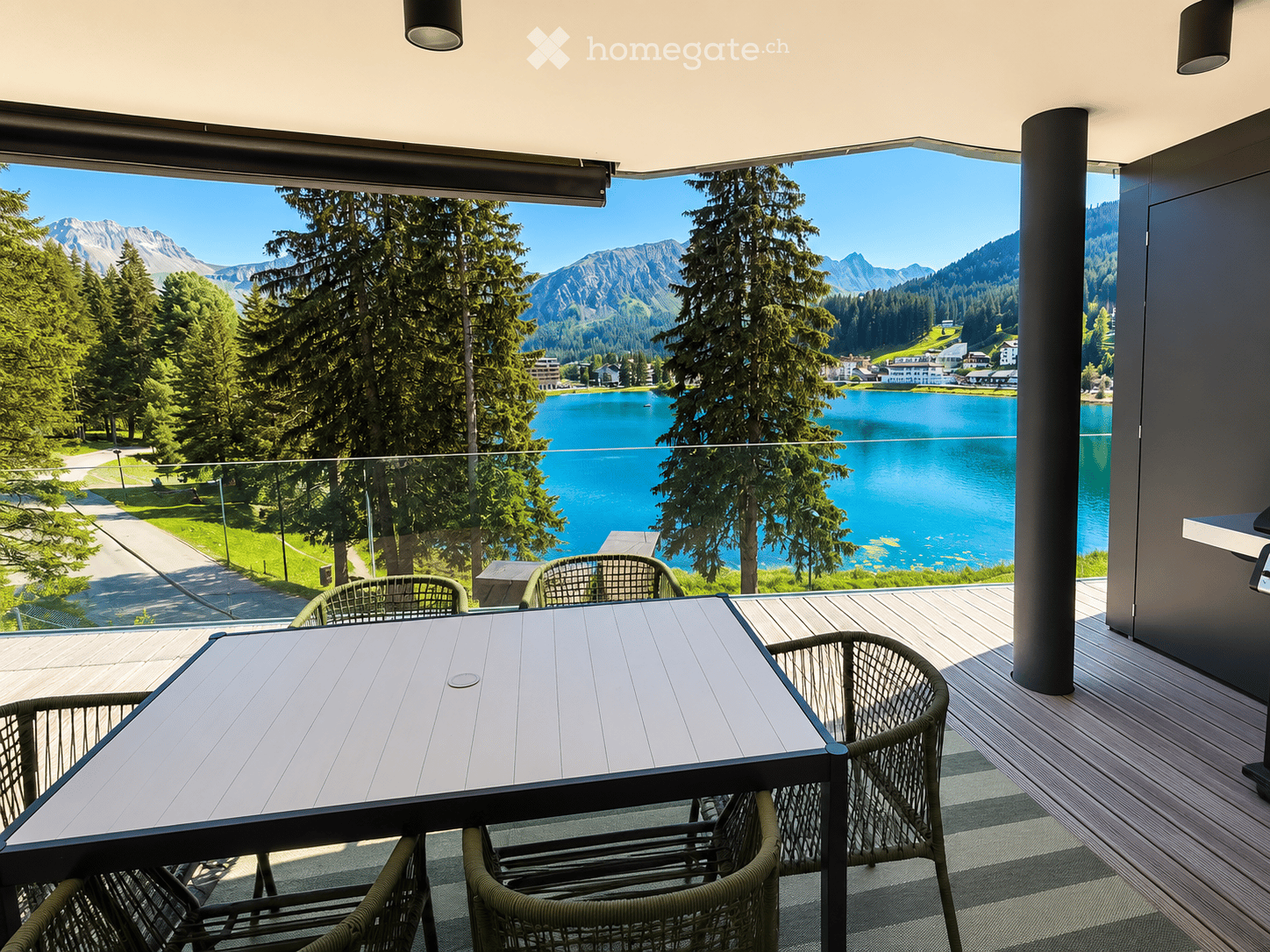 Balcony with a table and chairs, overlooking a scenic lake and mountain landscape.