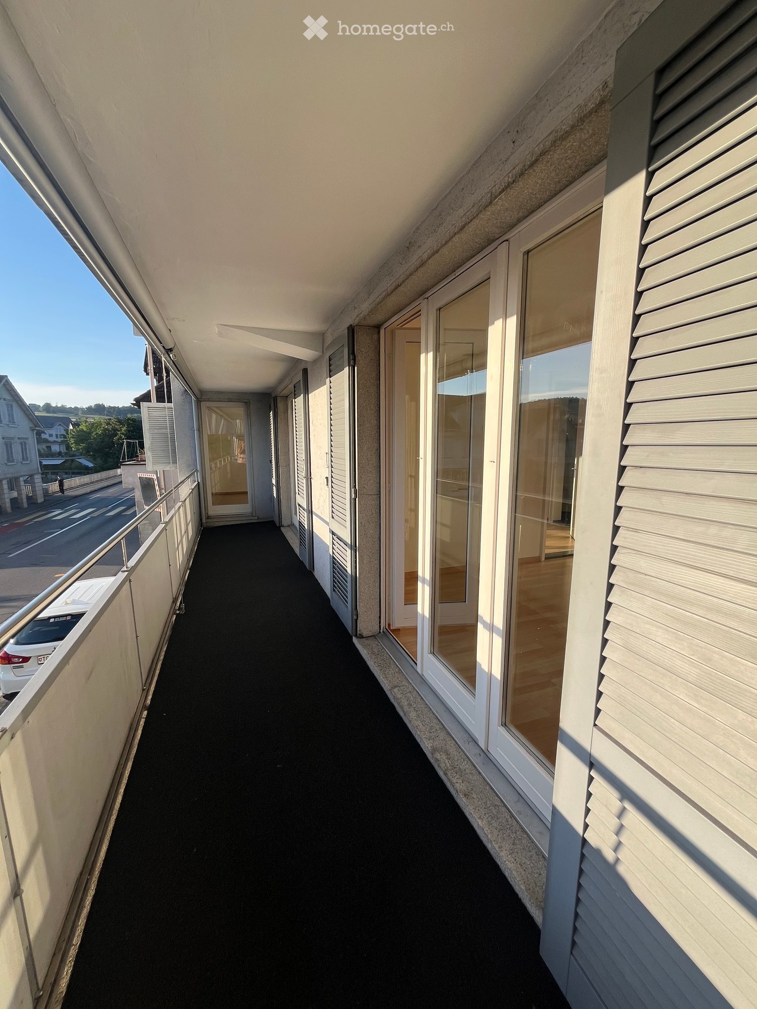 Balcony with black flooring, white railings, and large glass doors leading to an interior space.
