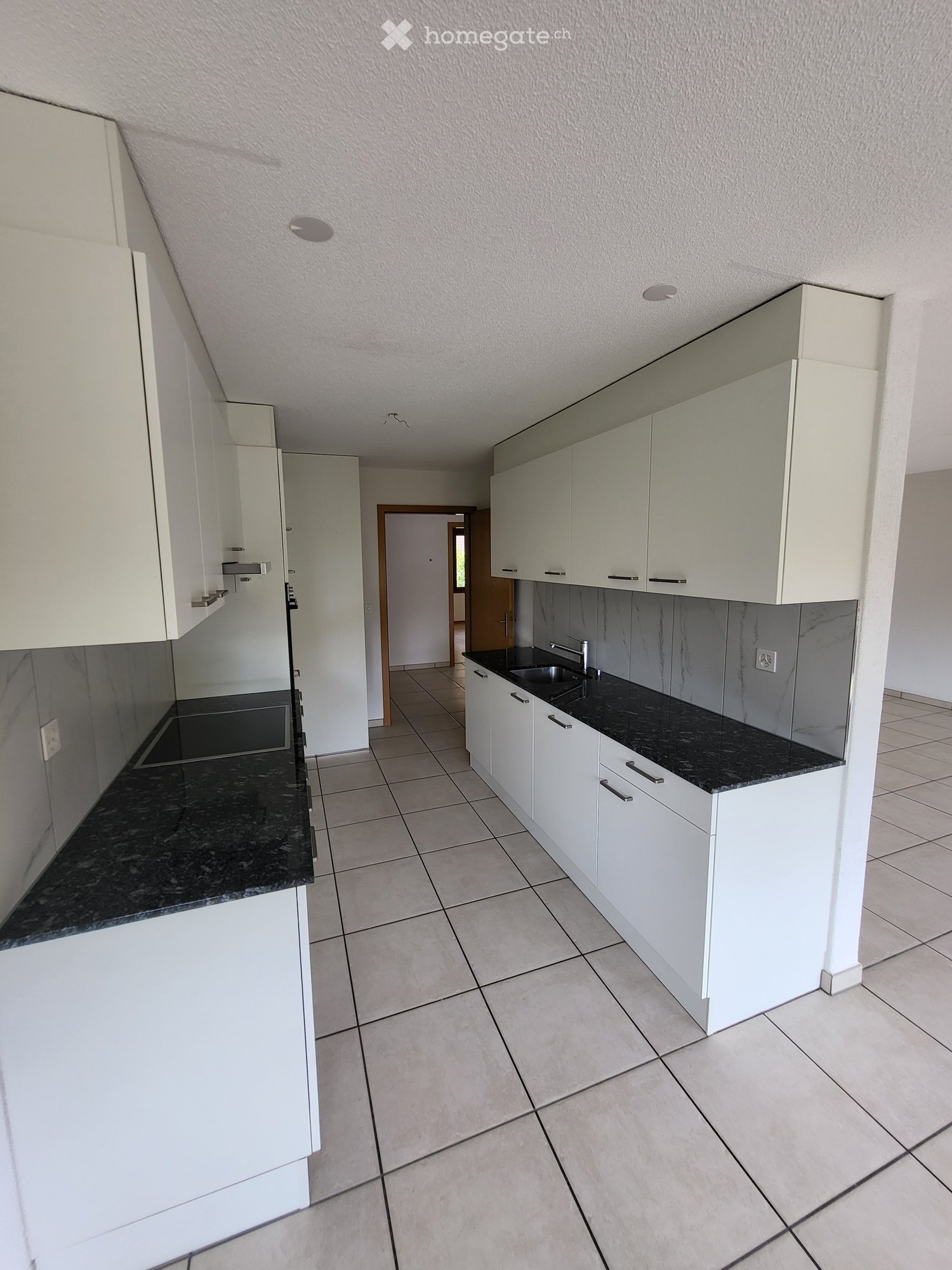 Modern kitchen with white cabinets, black granite countertops, tiled floor, and a sink with a faucet.