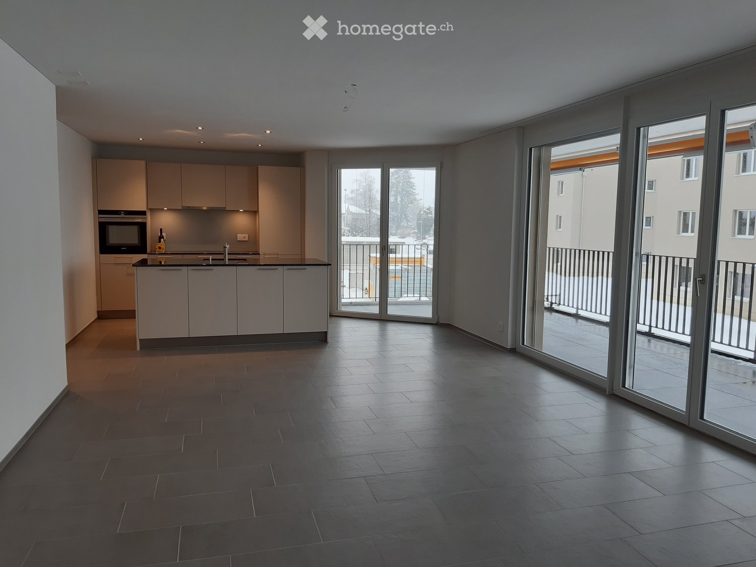 Modern kitchen with light-colored cabinets, a built-in oven, and a sink, connected to a spacious living area with large sliding glass doors leading to a balcony.