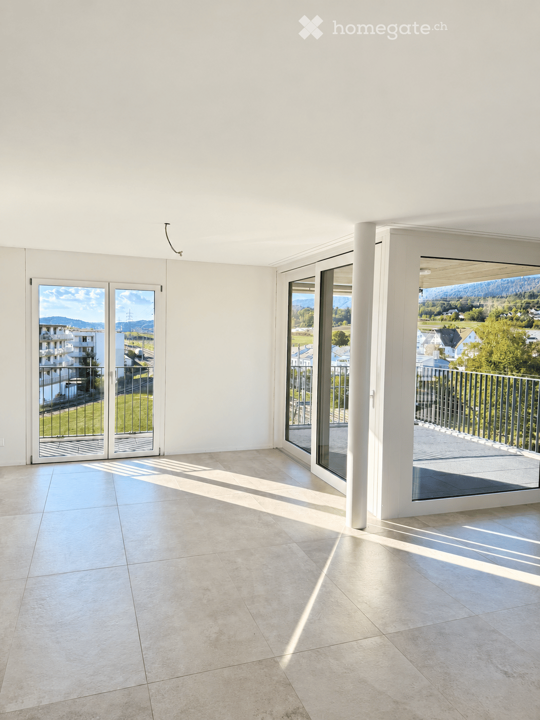 Bright, empty room with large glass doors leading to a balcony, tiled floor, and white walls.