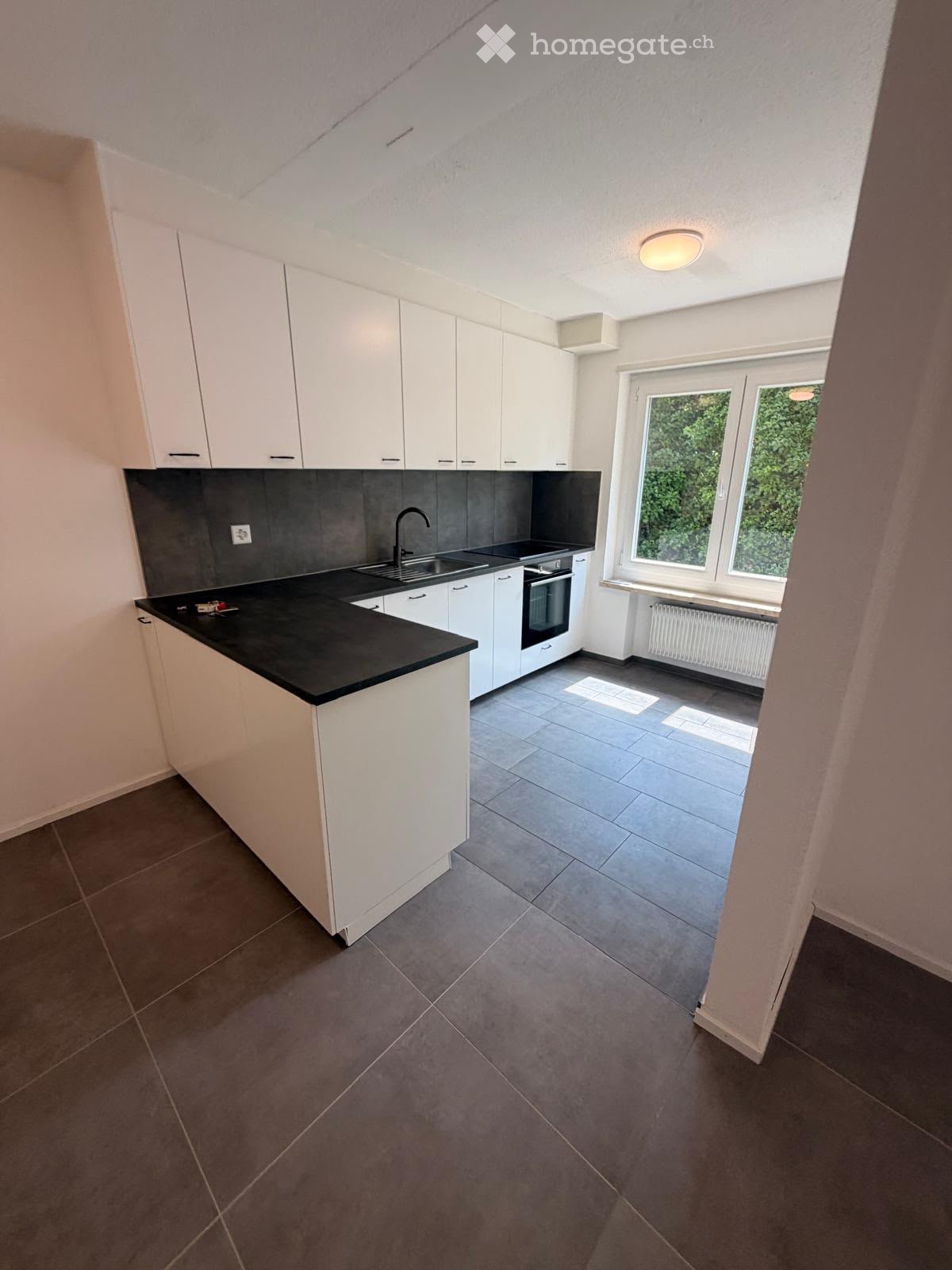 Modern kitchen with white cabinets, black countertop, sink, and oven. Large windows provide natural light.