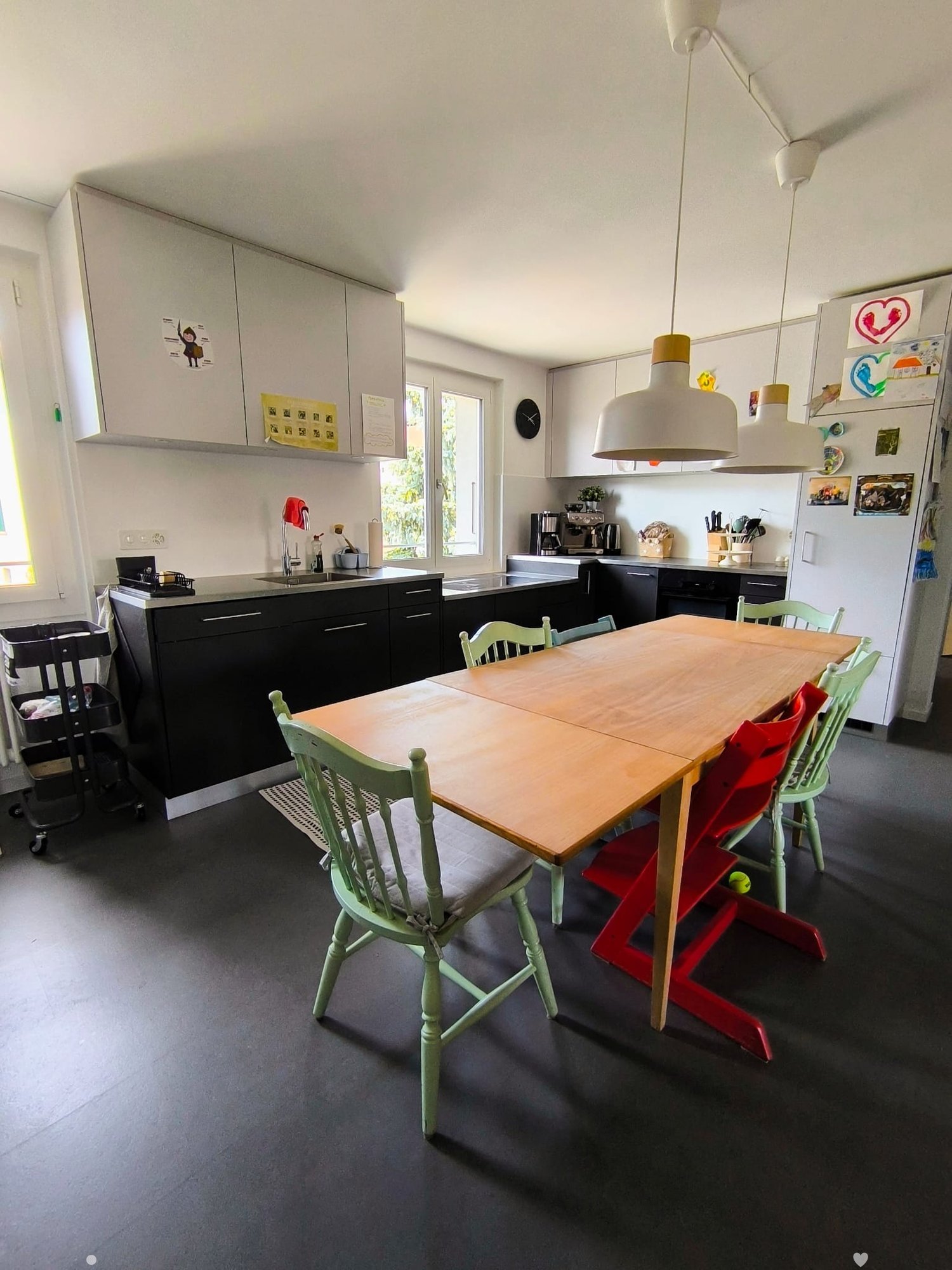 Modern kitchen with a wooden dining table and chairs, black cabinets, stainless steel appliances, and a sink area.