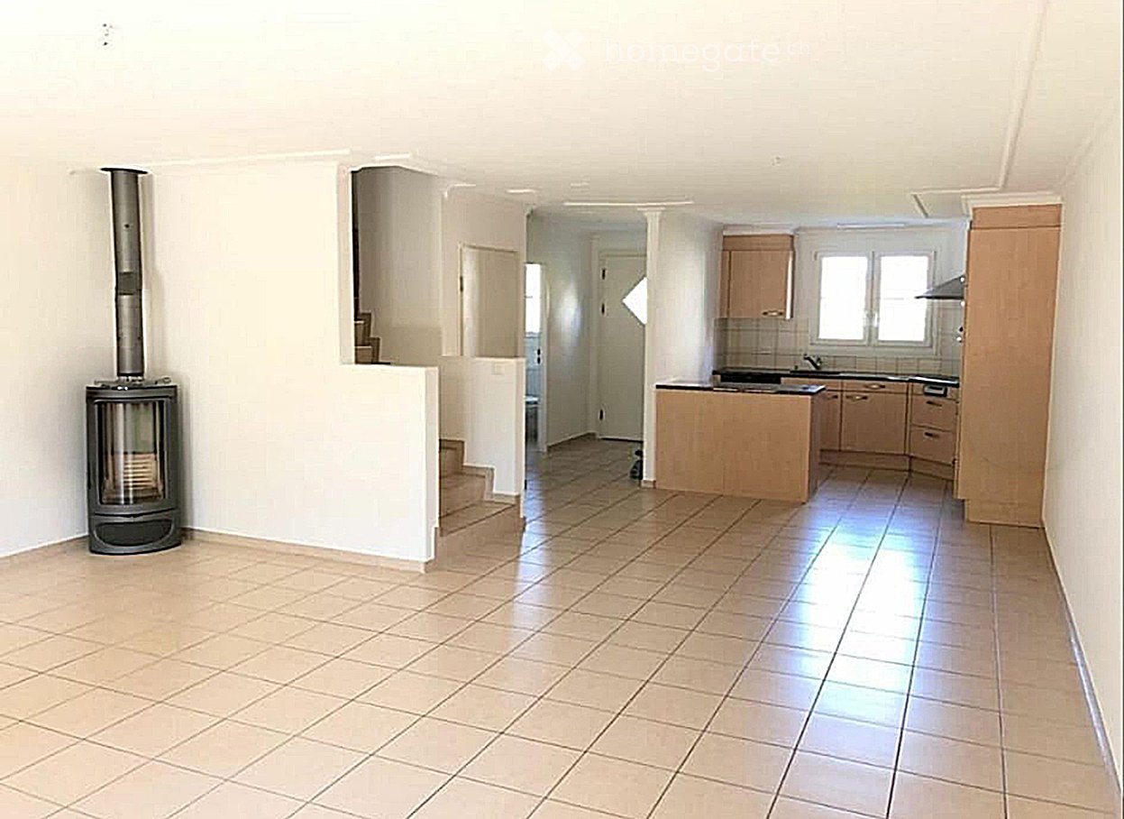 Open-plan living and kitchen area with tiled flooring, a fireplace on the left, and a kitchen island with cabinets and a sink.