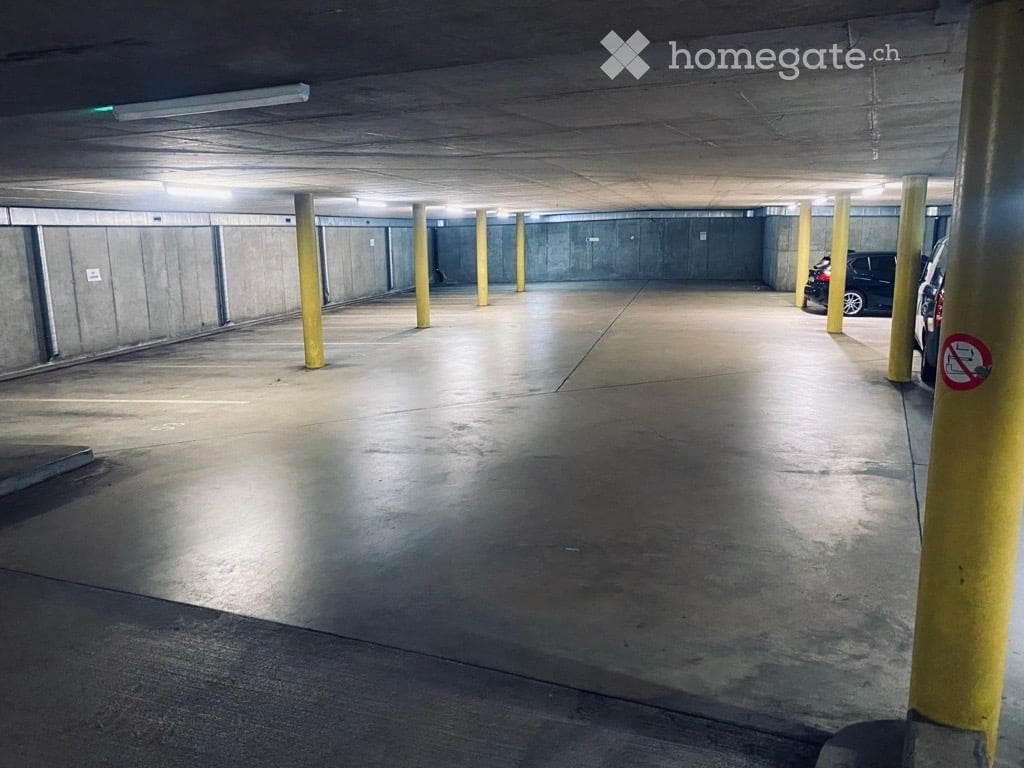 Underground parking area with concrete floors and walls, yellow support pillars, and a few parked cars visible in the background.