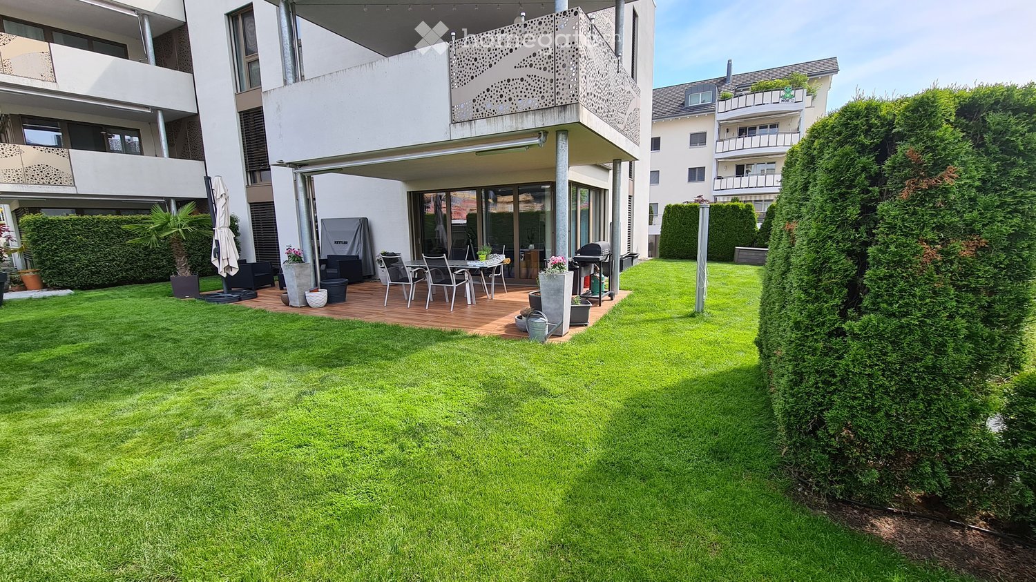 Well-maintained garden with a wooden deck, outdoor furniture, grill, and potted plants.
