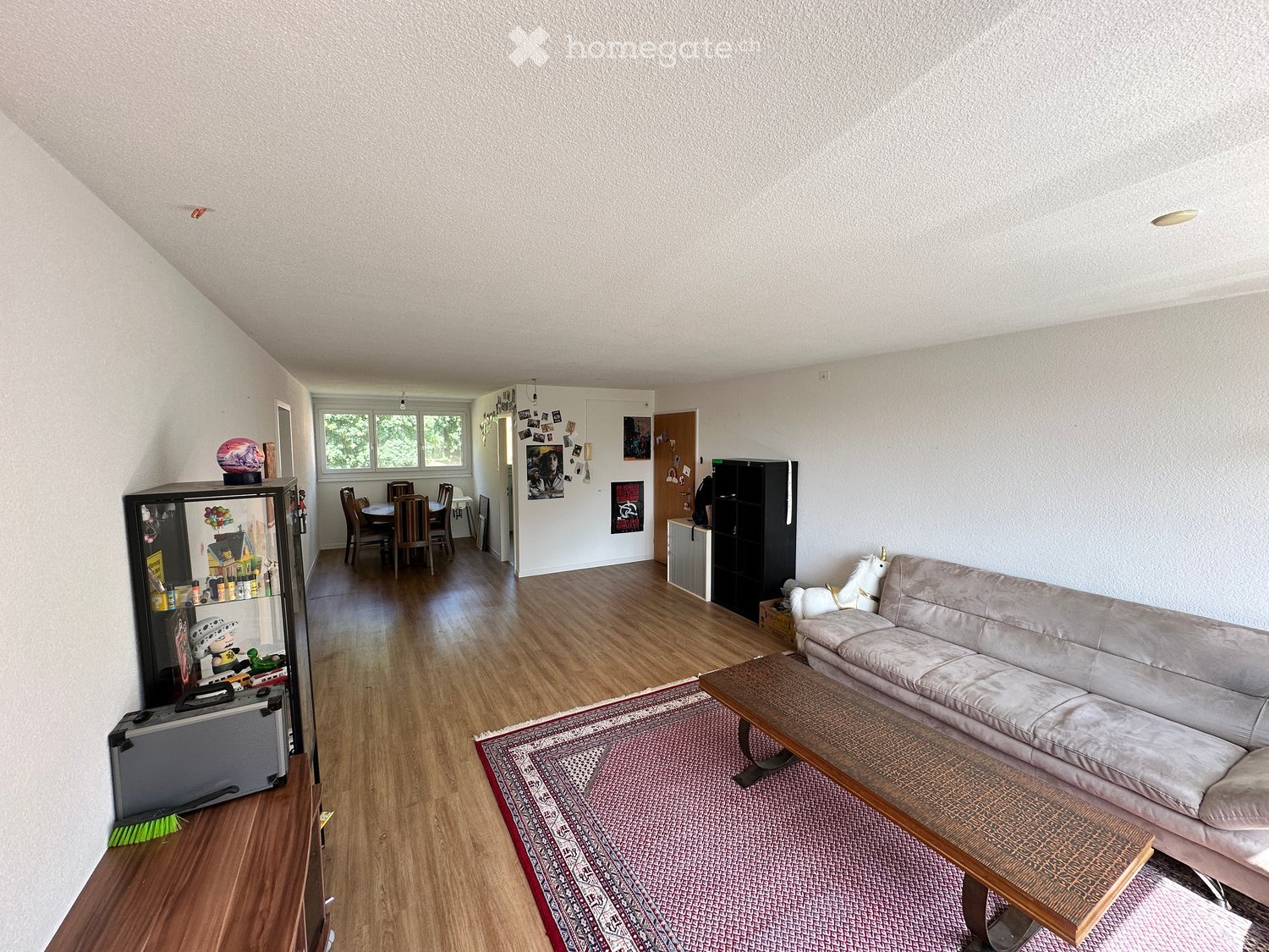 Living room with a sofa, coffee table, dining area with a table and chairs, and a refrigerator with toys displayed on it.