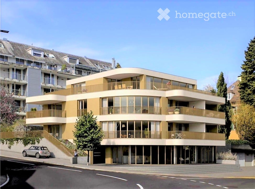 Modern multi-story building with curved balconies and large windows, featuring a raised ground floor and a staircase leading up to the entrance.