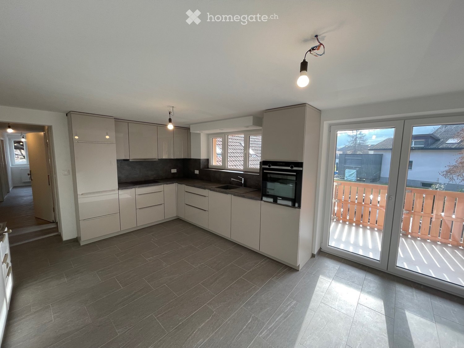 Modern kitchen, white cabinets, granite countertops, stainless steel appliances, grey tiled floor, sliding glass doors to balcony, overhead lighting